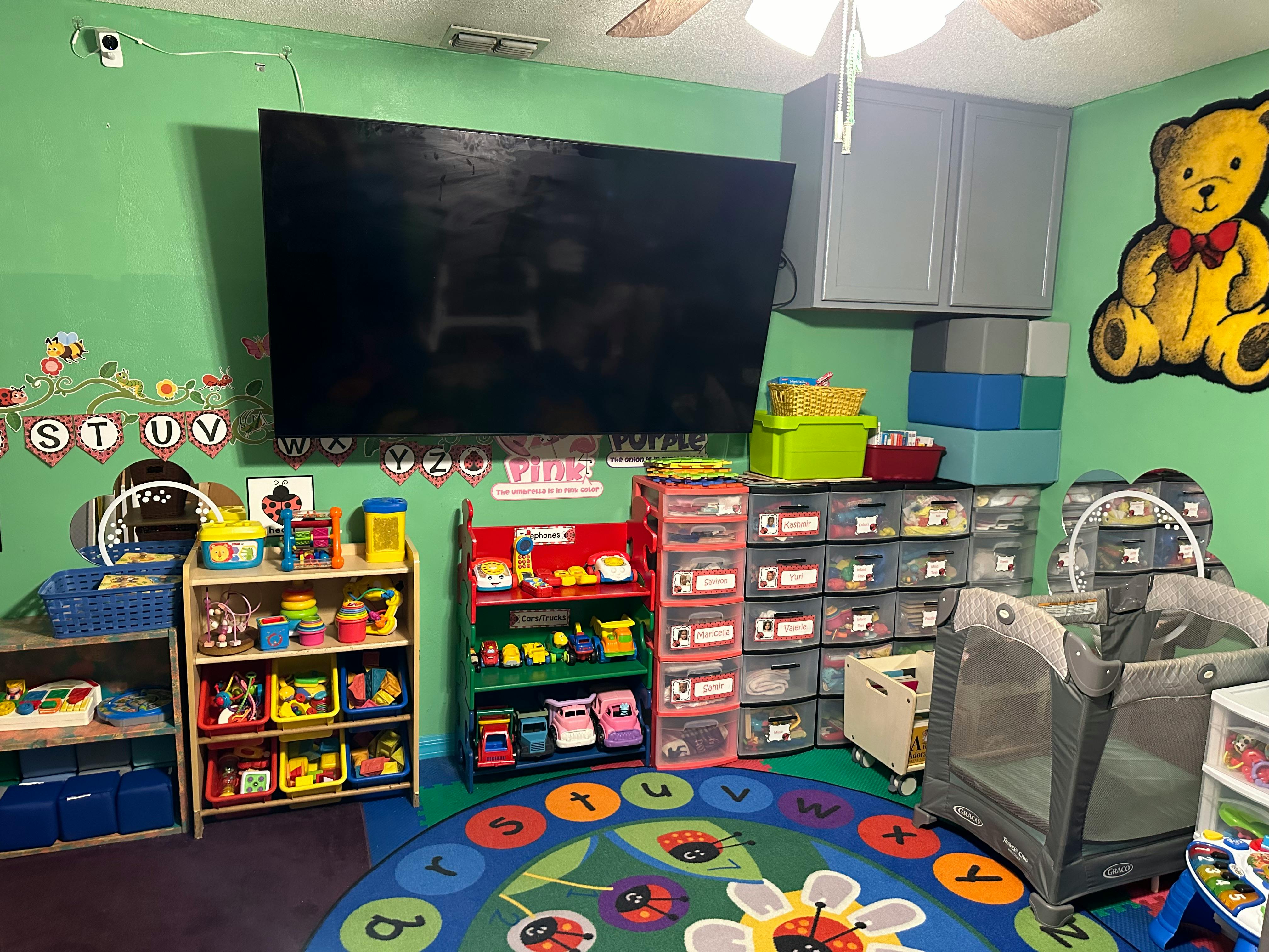 A room with a large television, shelves of toys, and a playpen