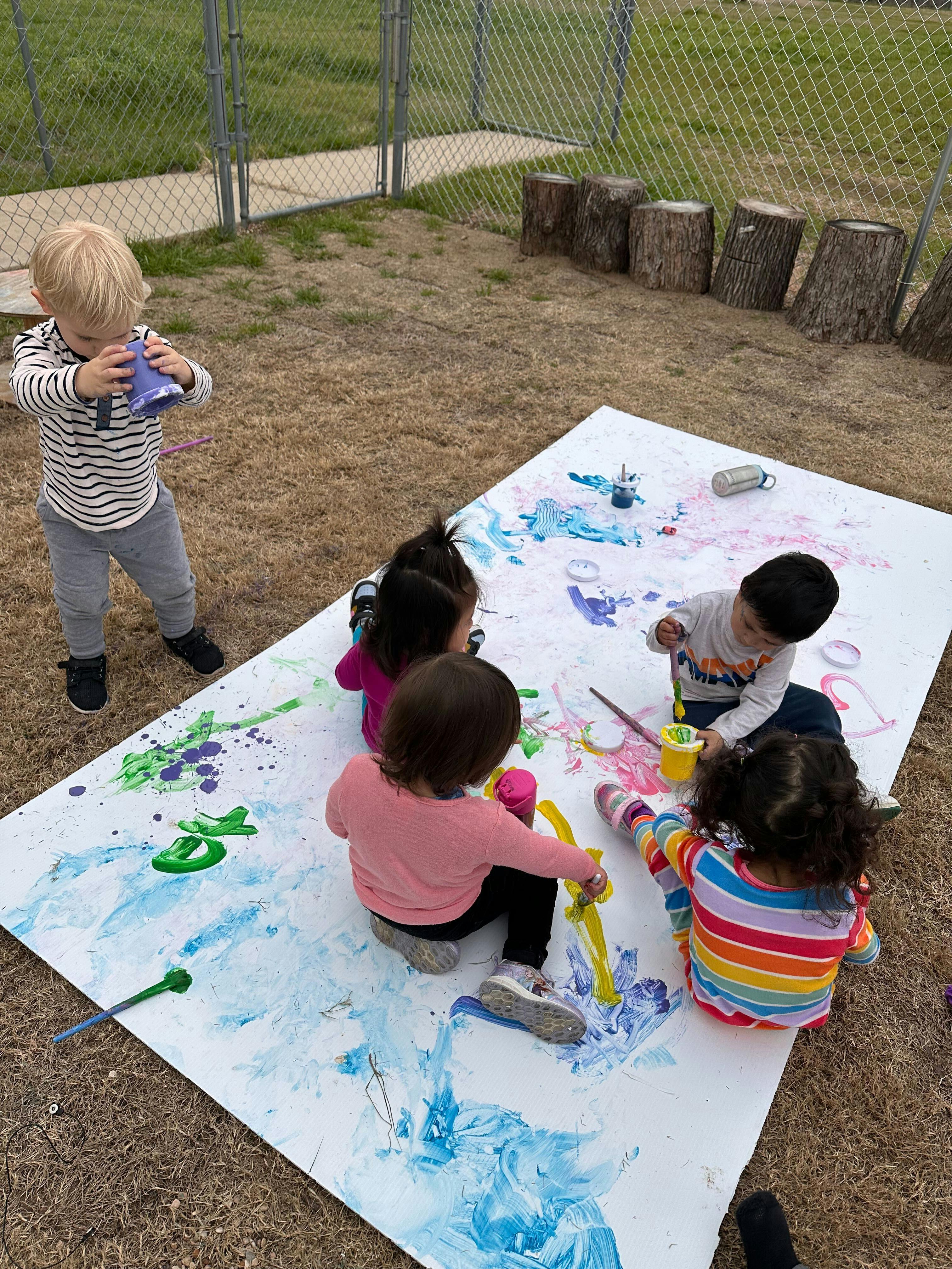 Children painting on a large white sheet outdoors