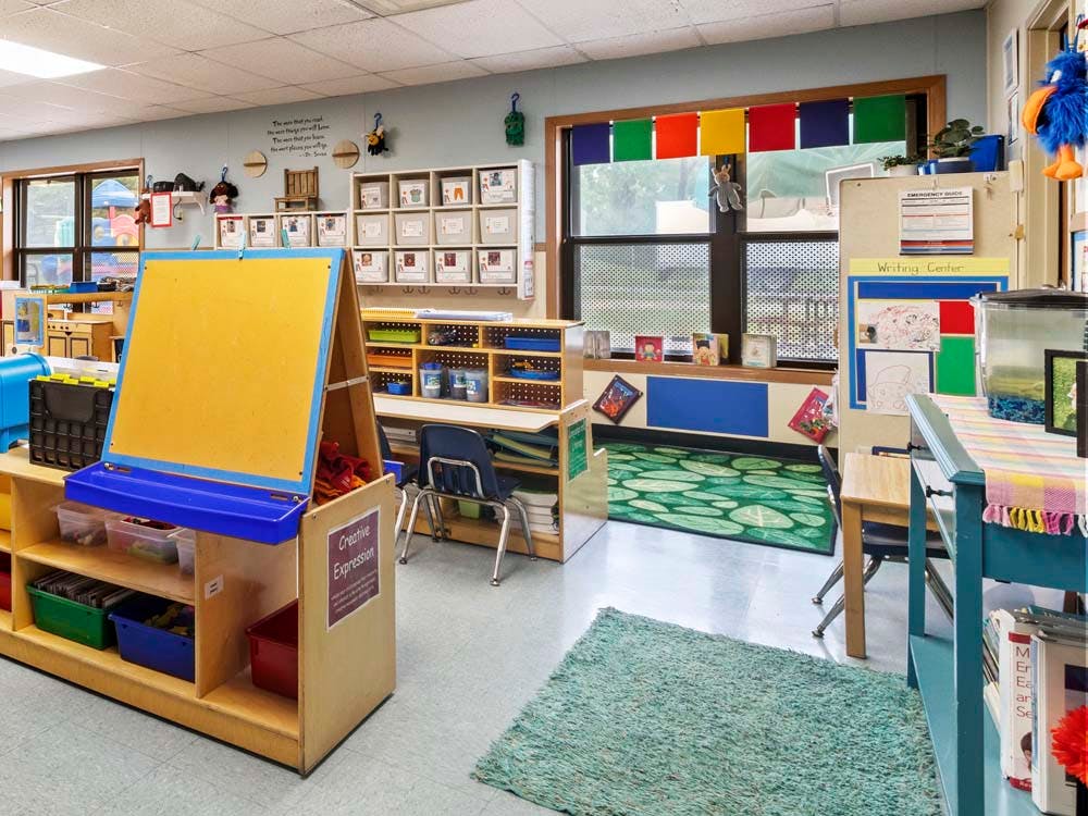An empty early childhood classroom with an easel, shelving, and rugs