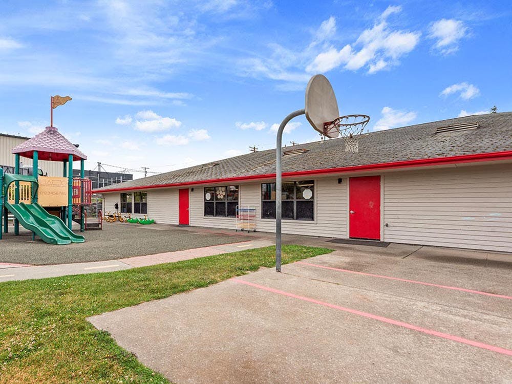 Playground with swings and slides next to a building and basketball hoop