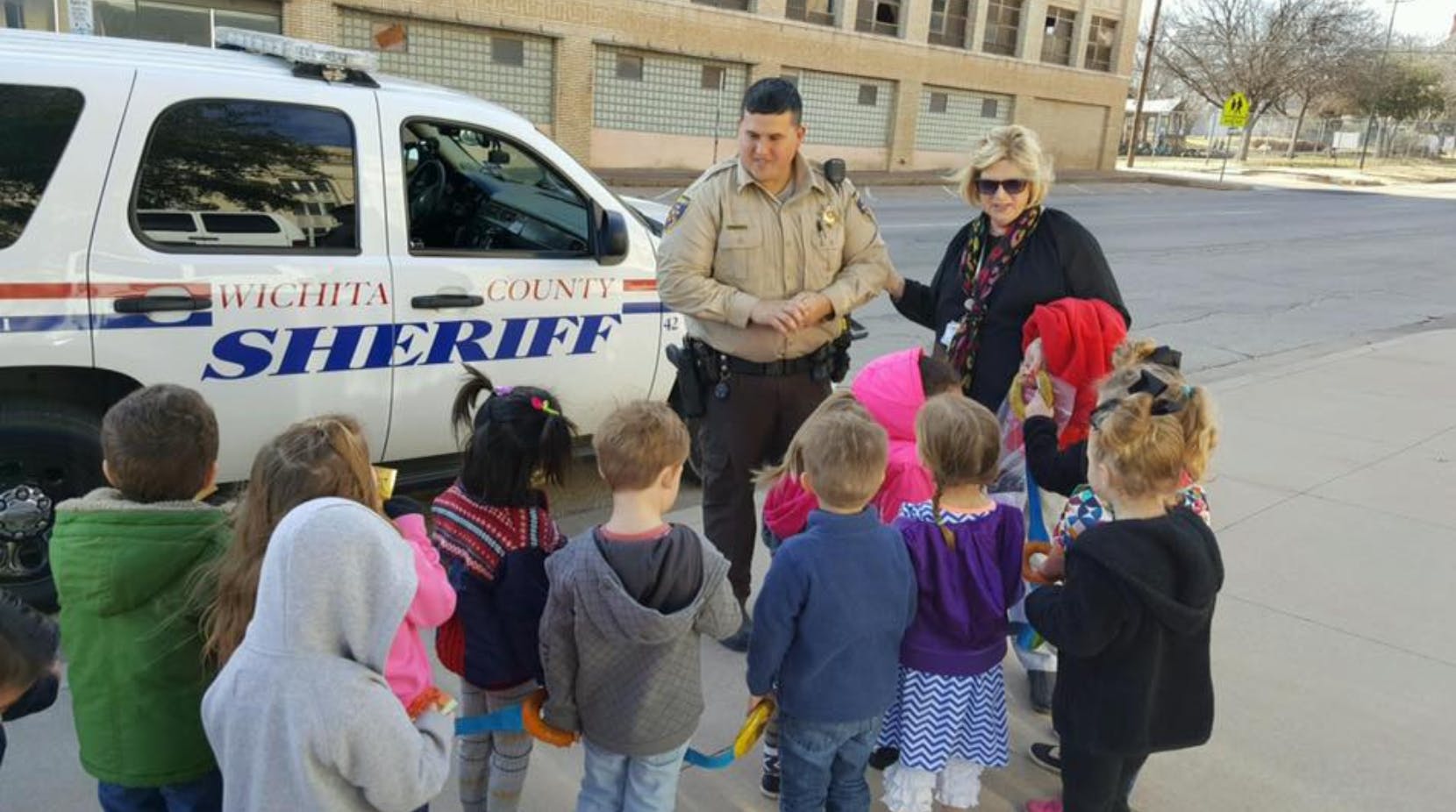 Sheriff and person with a group of children next to a sheriff vehicle