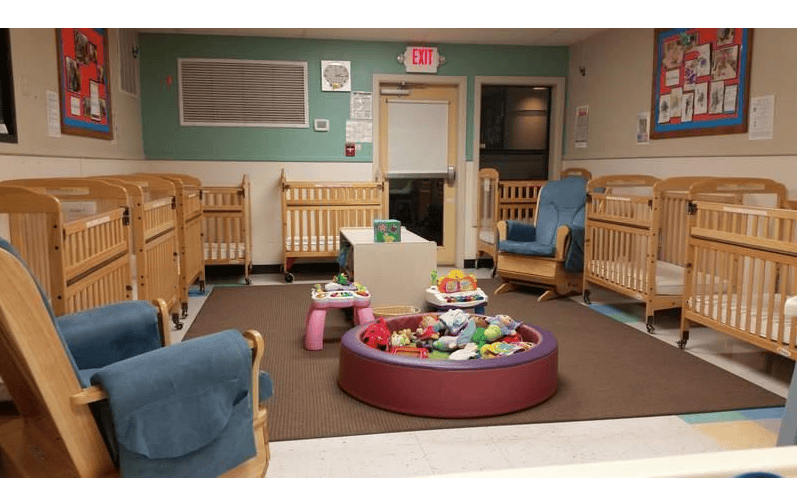 A room with several cribs, two rocking chairs, and toys in a playpen