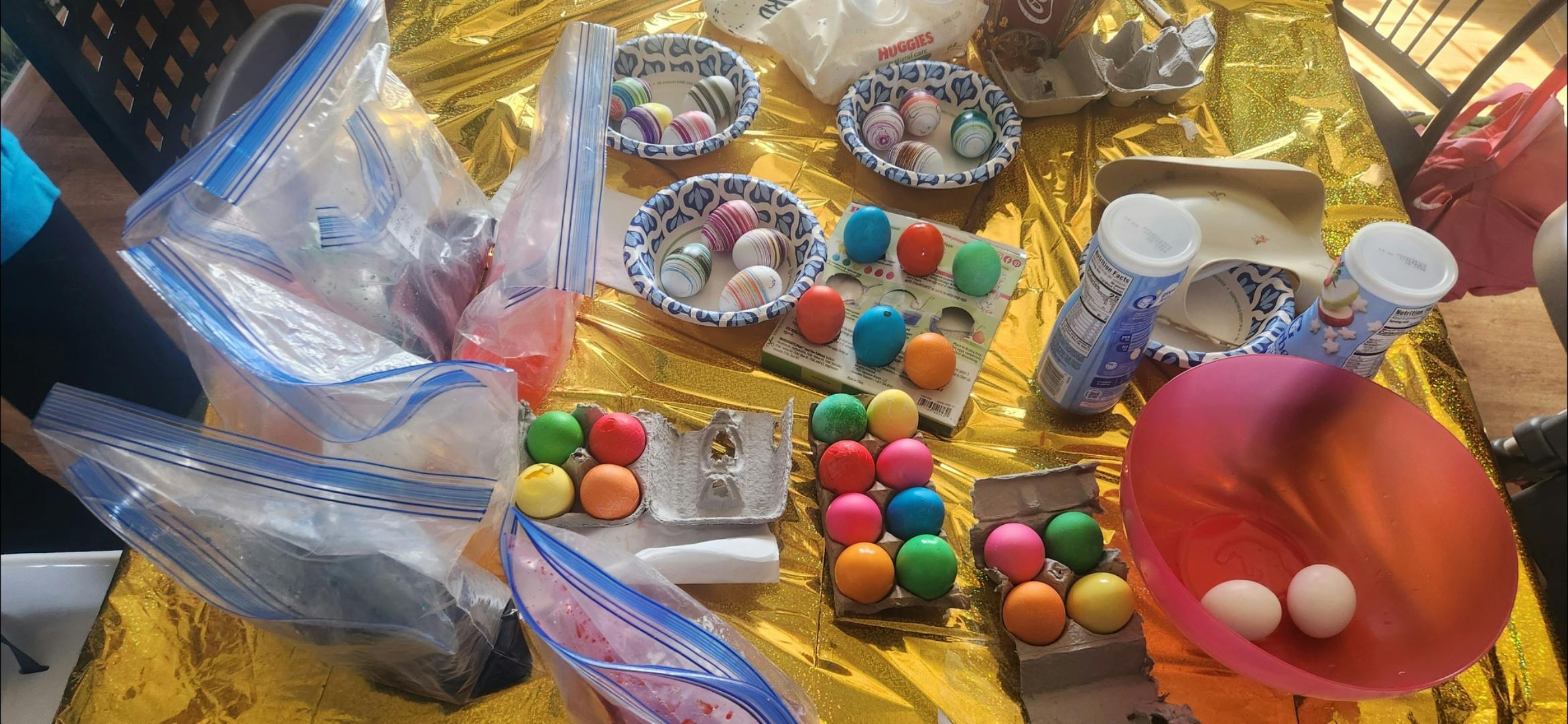 A table covered in gold with many colorful dyed eggs in cartons and bowls