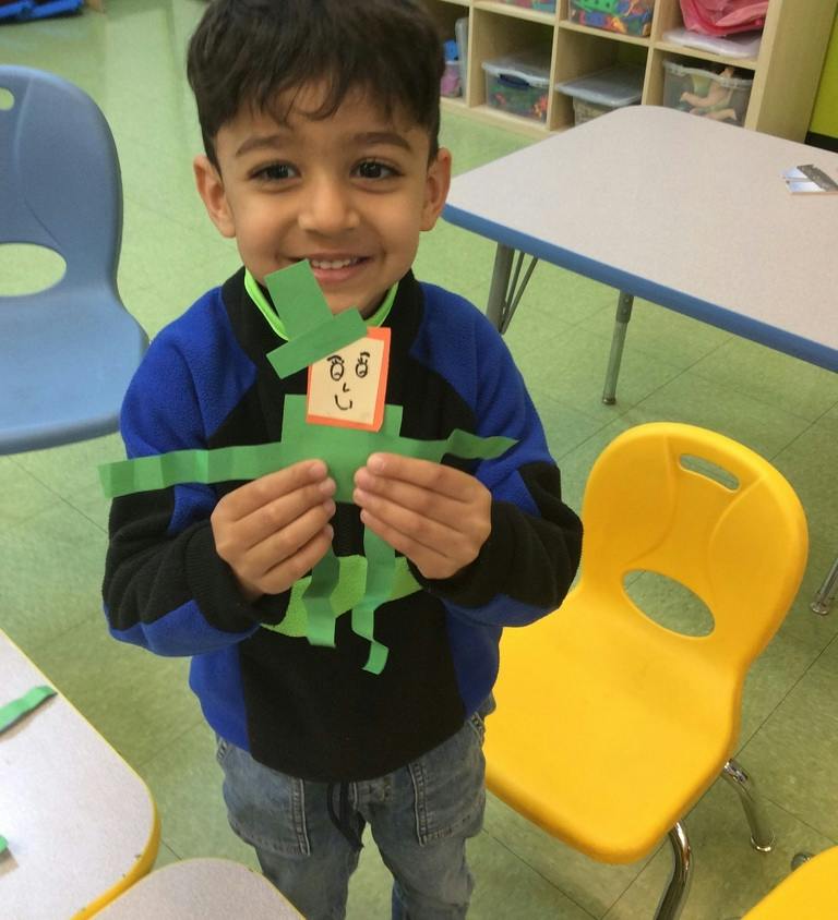 Child holding a paper craft figure in a classroom