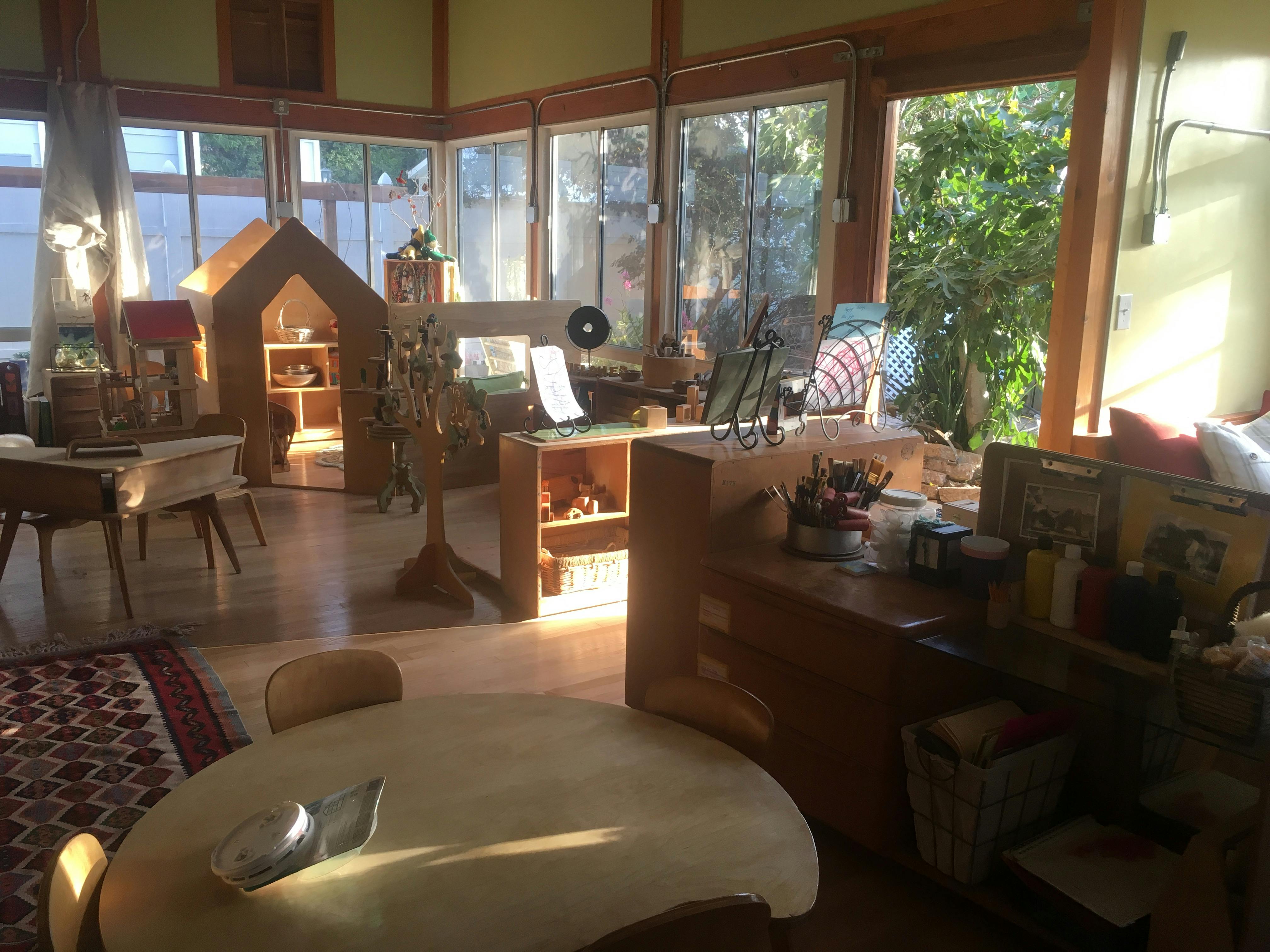 Classroom with large windows, wooden furniture, and a small table in-door playhouse