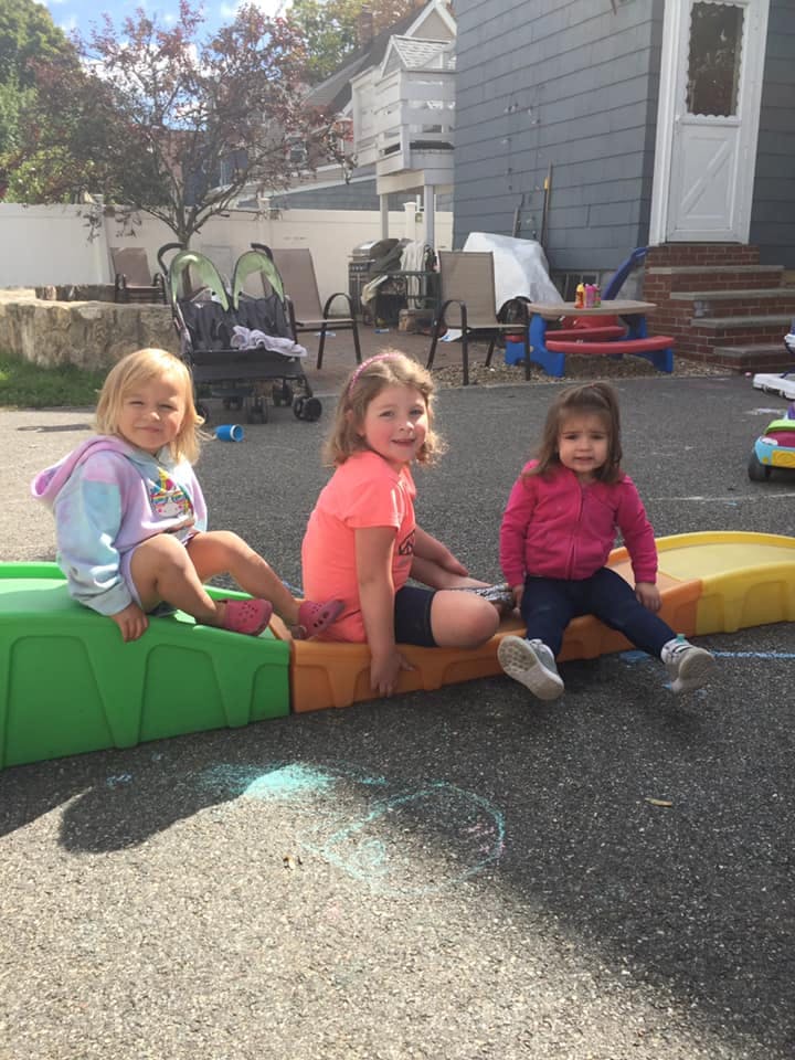 Three children sitting on a low plastic play structure outdoors