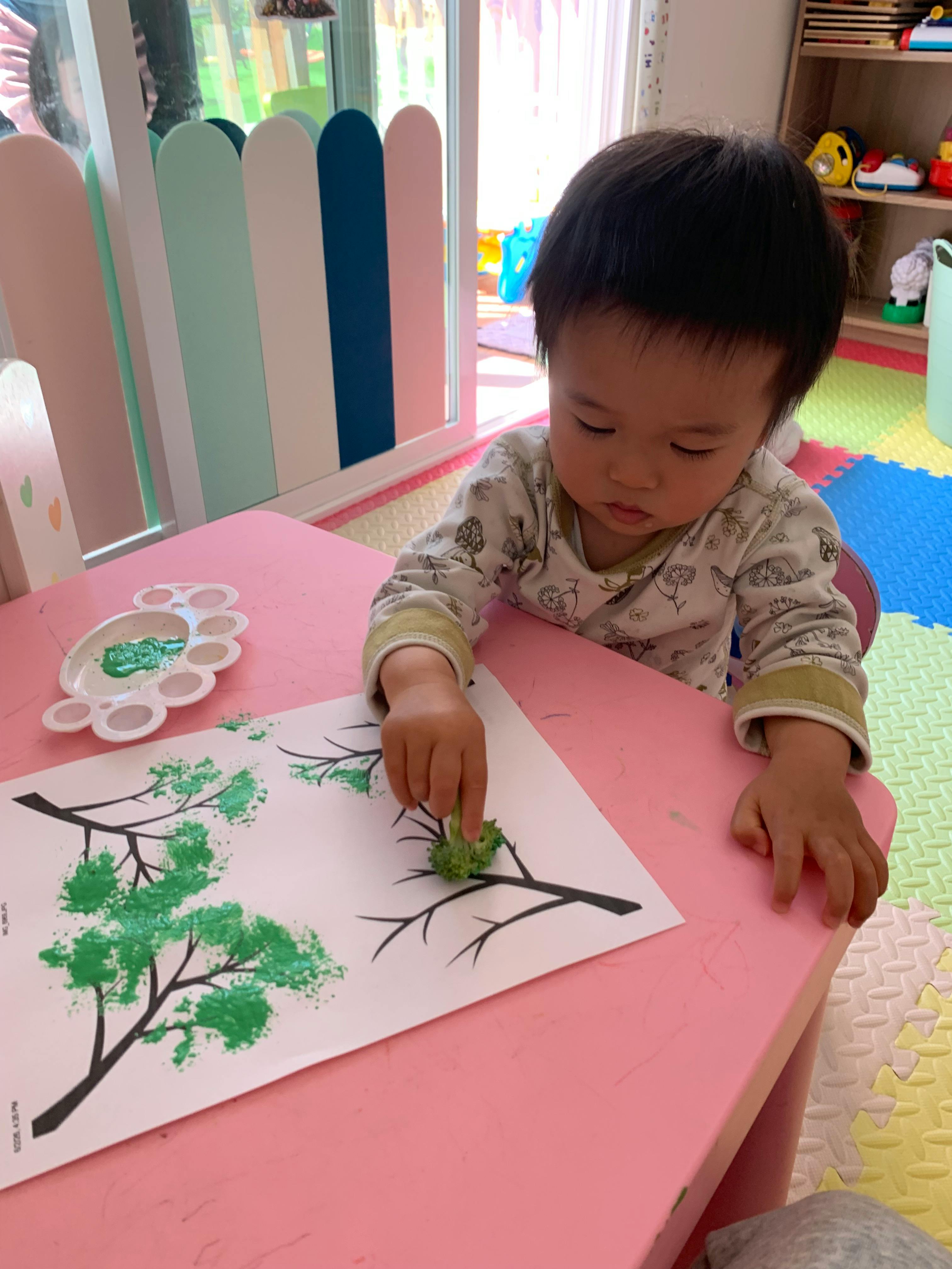 Child painting a tree on paper using broccoli dipped in green paint