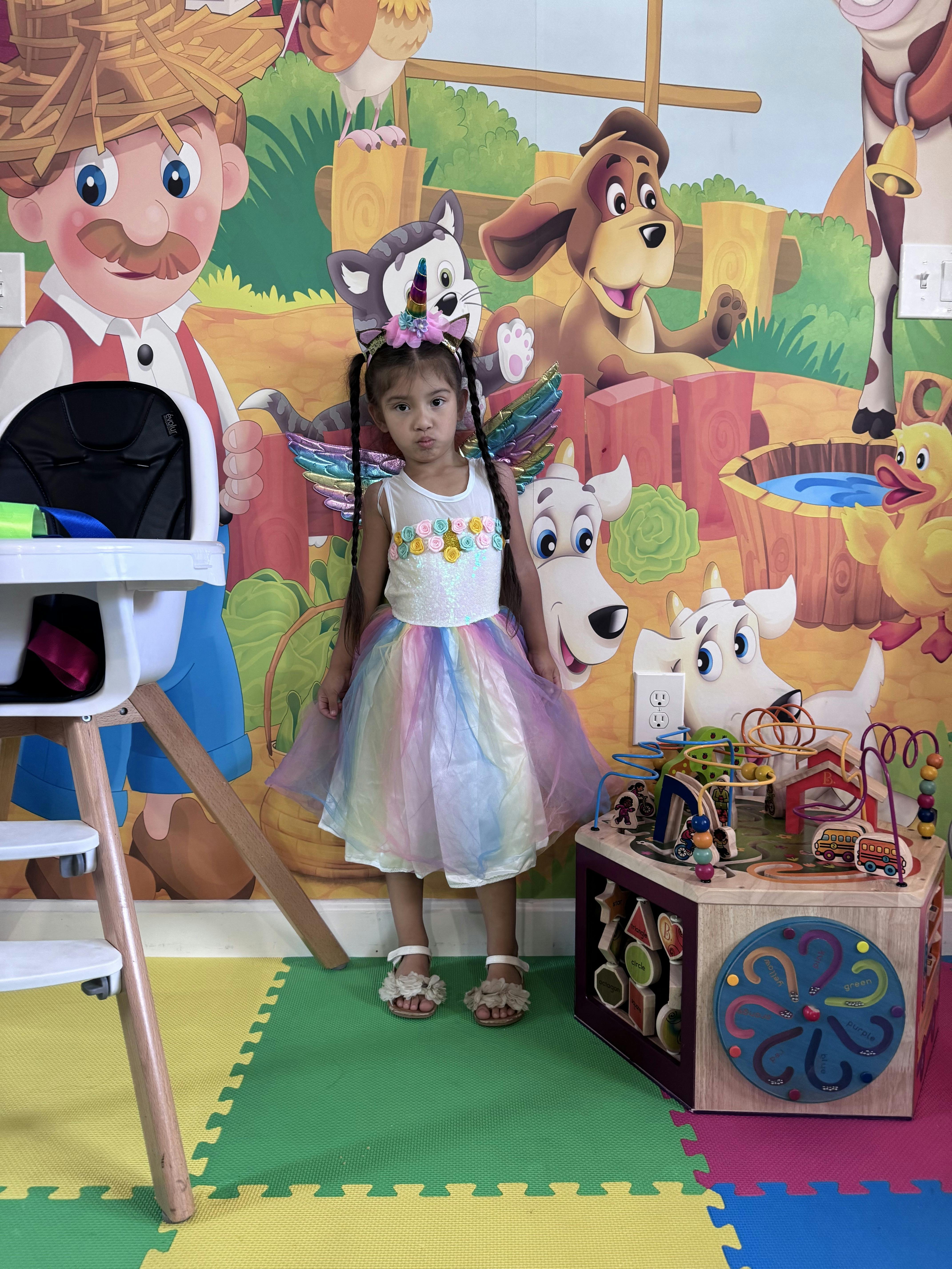 Child in a rainbow dress and animal headband standing in a room with cartoon murals