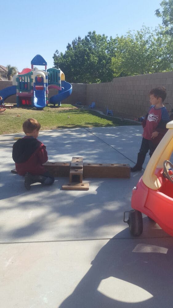 Two children playing with a wooden structure and a toy car outdoors