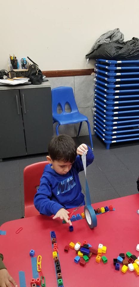 Child playing with tape and colorful blocks at a red table