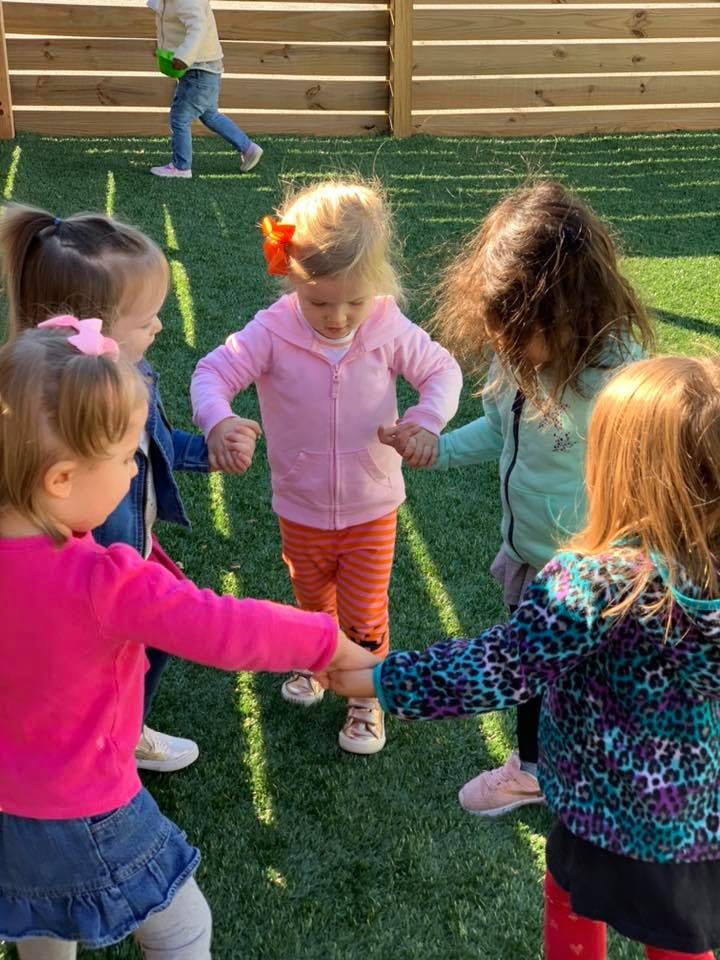 Four children holding hands in a circle on artificial grass