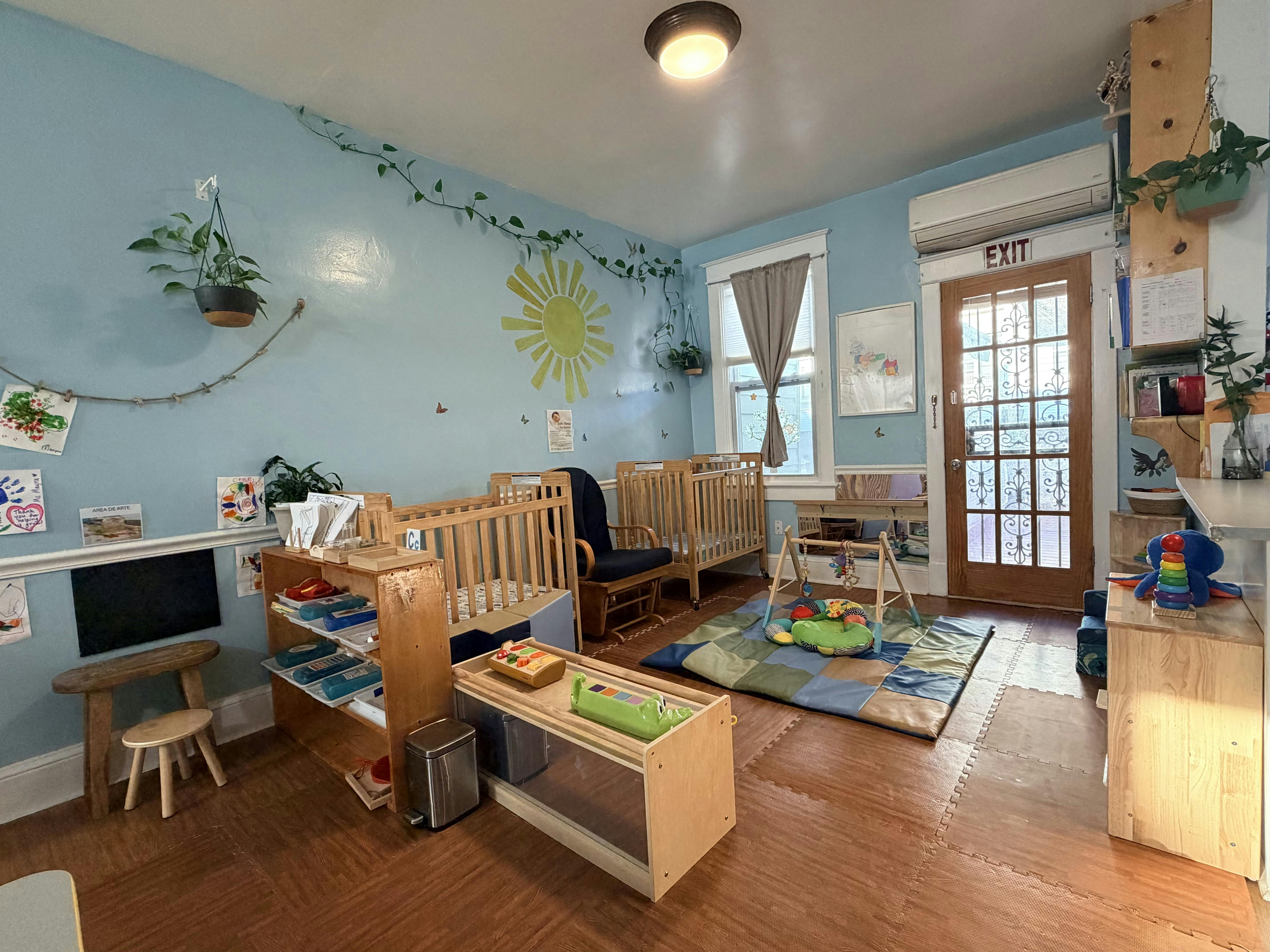 Childcare room with cribs, play mat, and educational toys