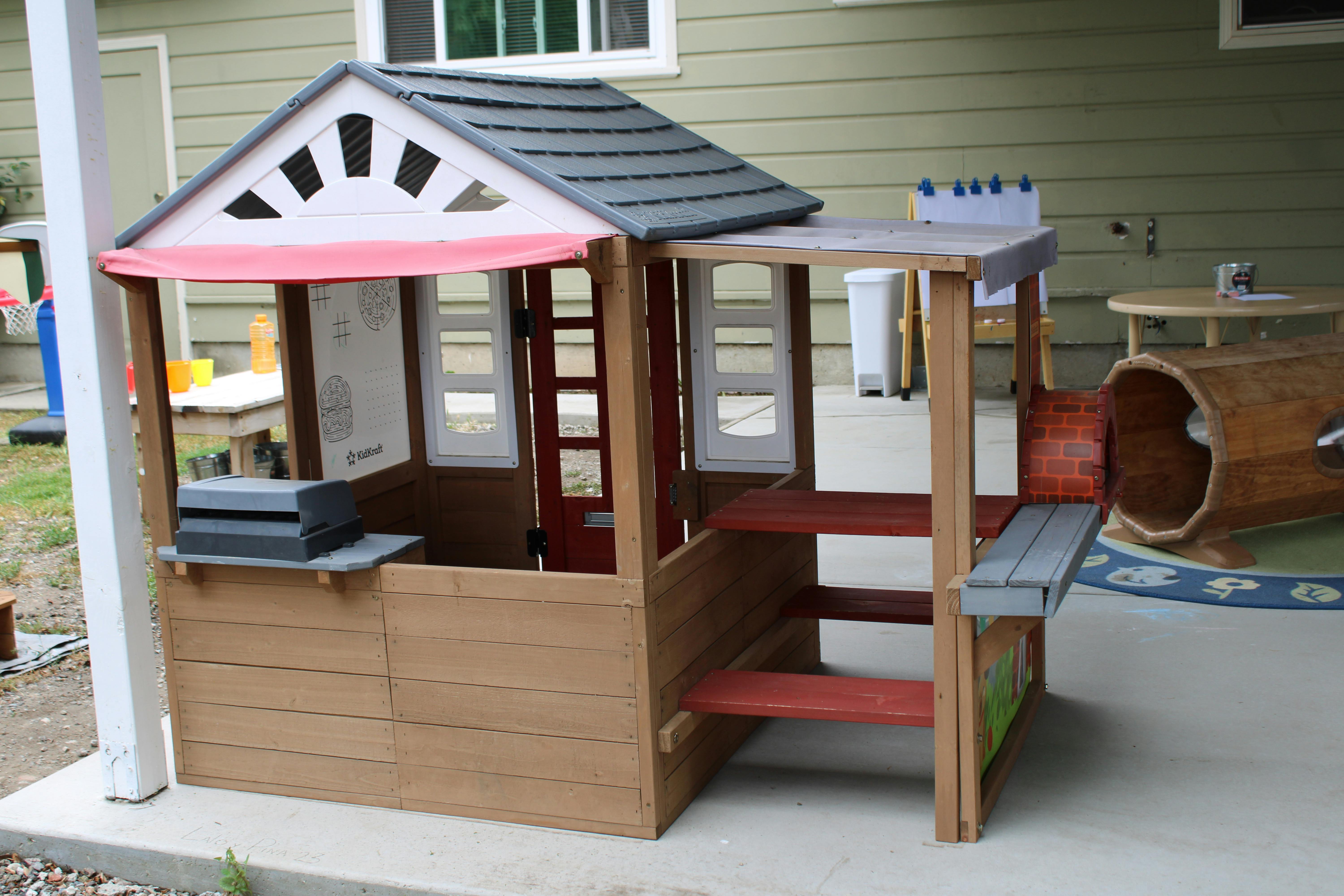 Wooden playhouse with a red awning and attached picnic table