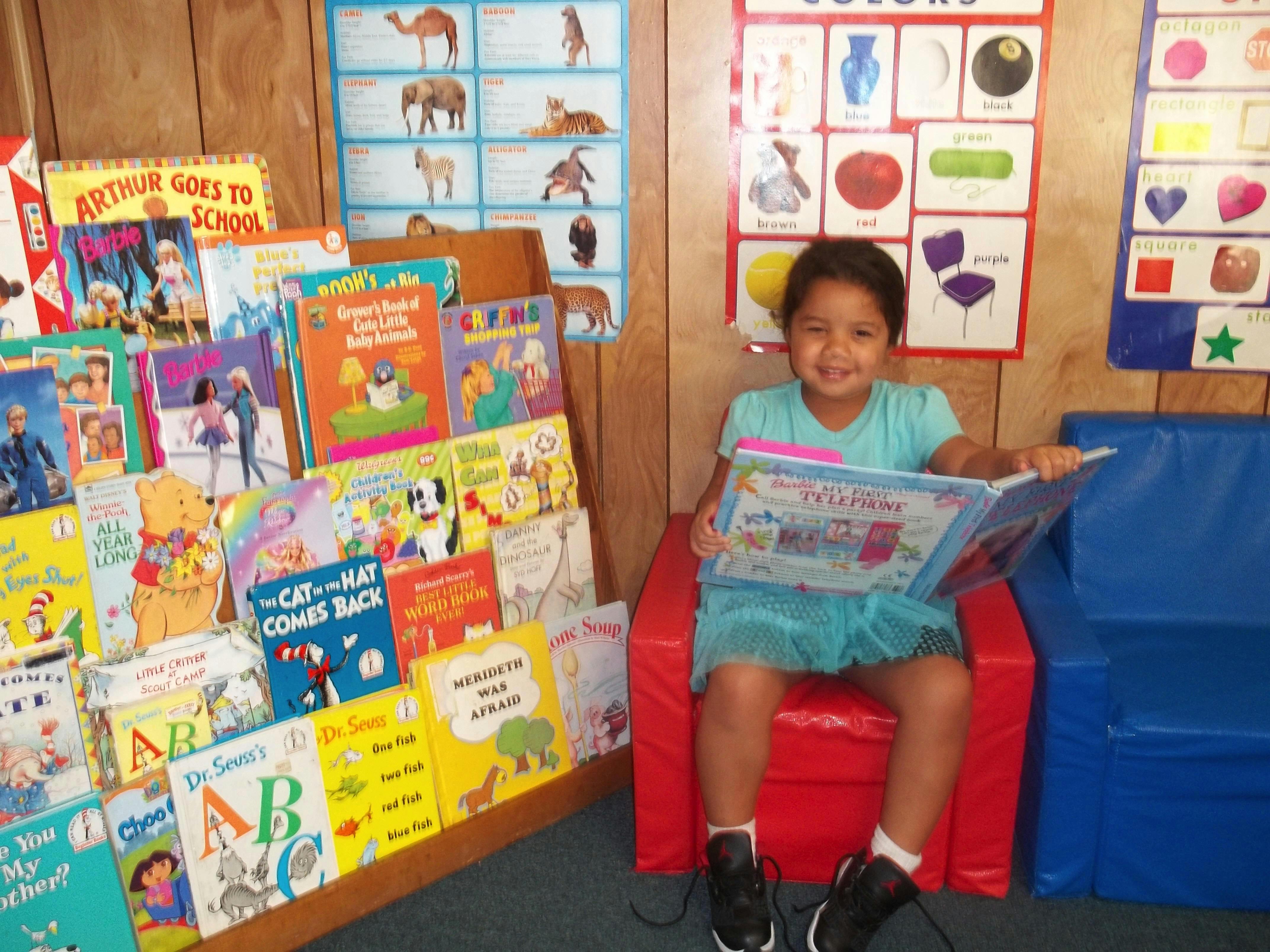 Child sitting in a red chair reading a book in a classroom