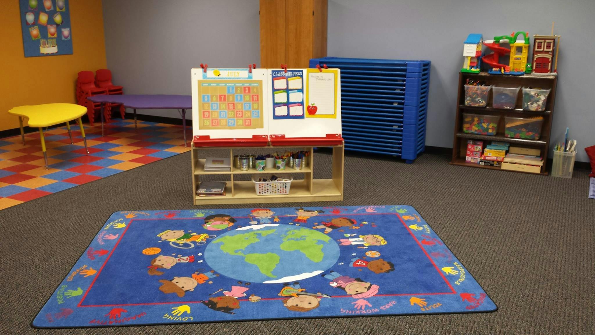 Classroom with a world map rug, easel, and shelves with colorful tables and chairs