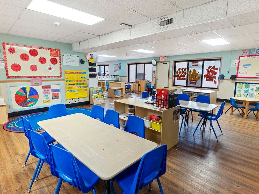 An empty classroom with tables and blue chairs
