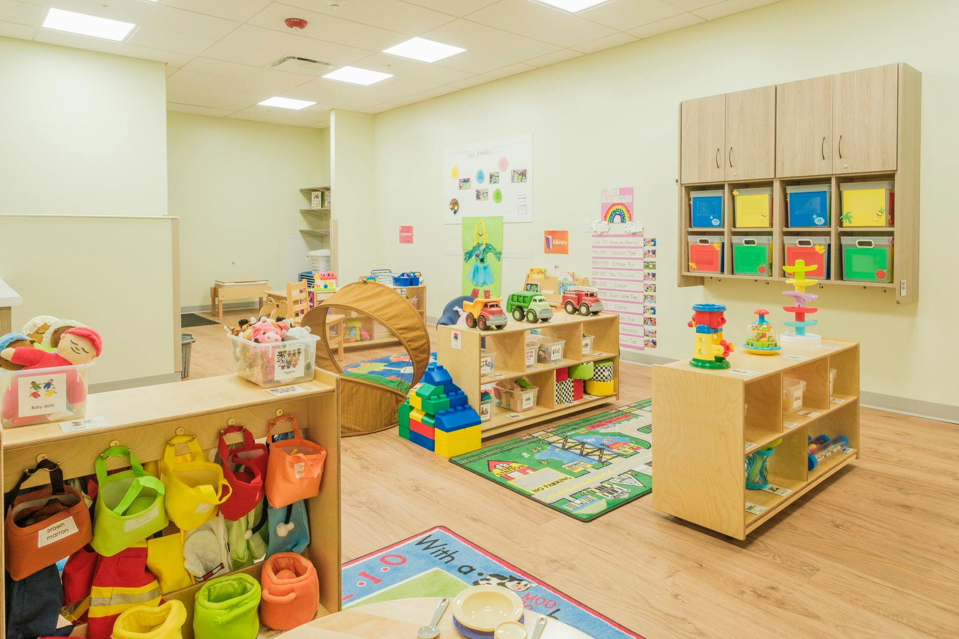 Childcare classroom with toys, play tunnel, dress-up clothes, and storage units
