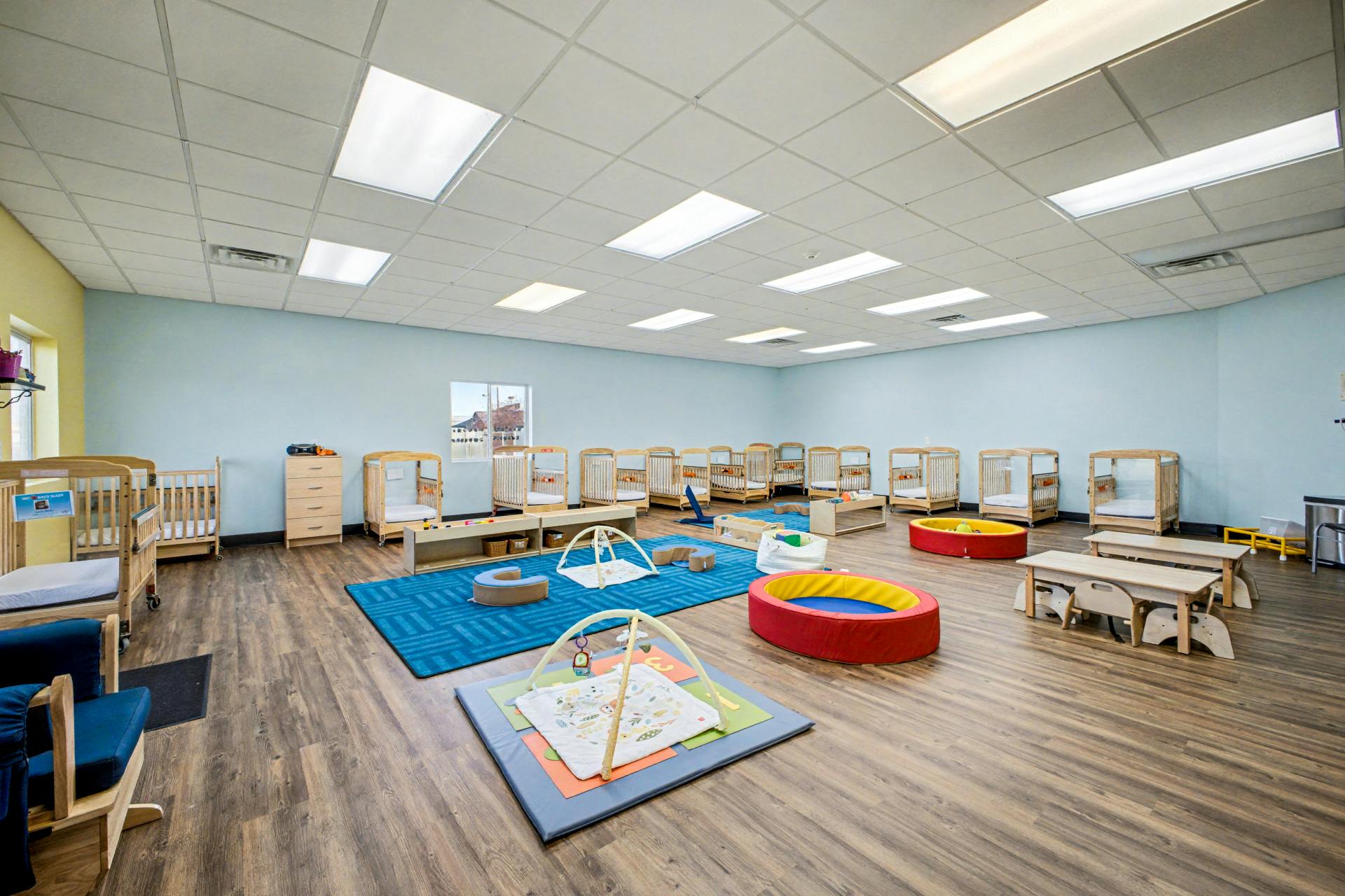 A daycare room with multiple cribs, activity mats, and small tables