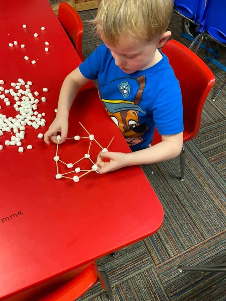Child building a structure with toothpicks and marshmallows on a red table