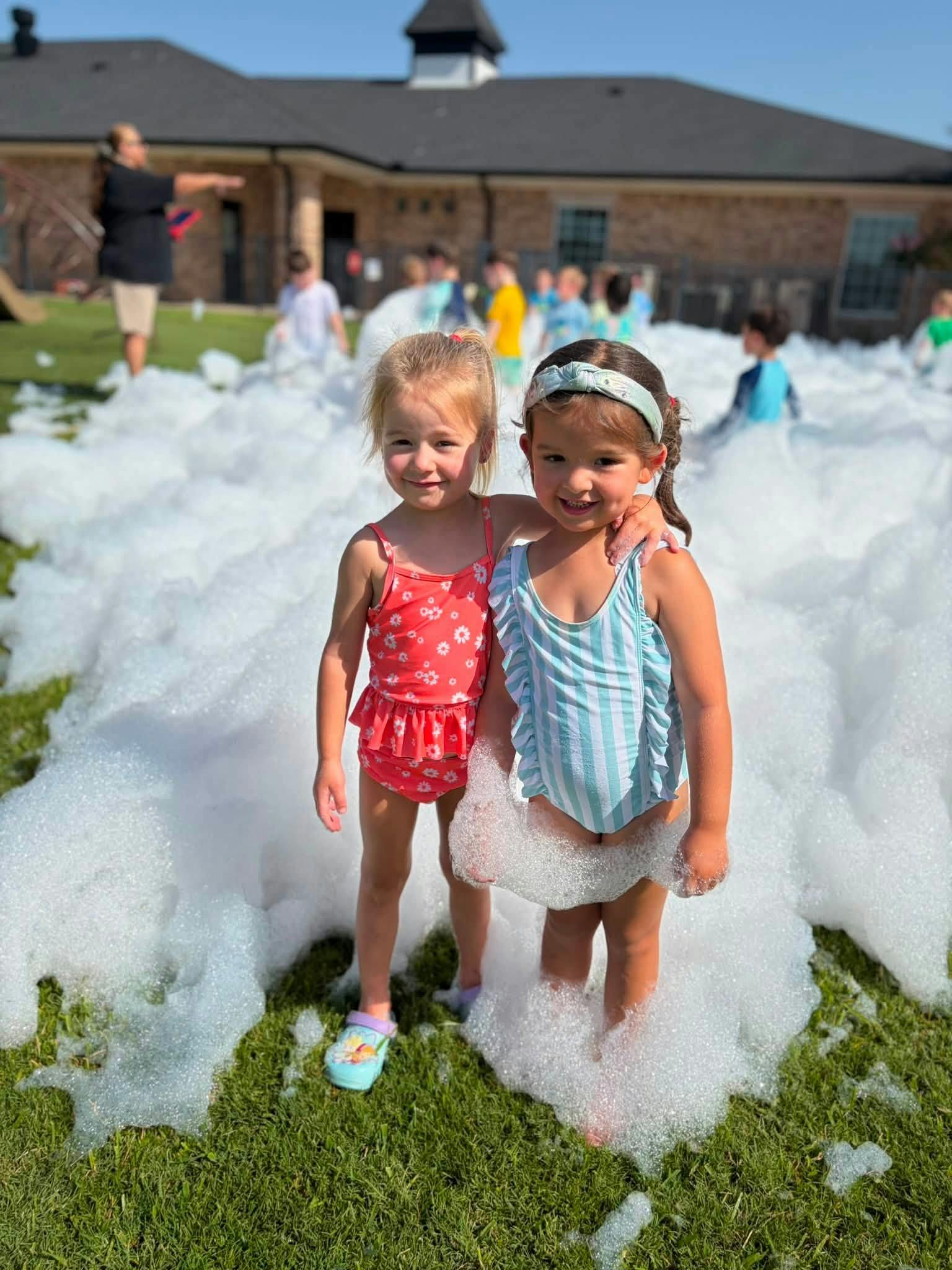 Two children standing in foam on a lawn