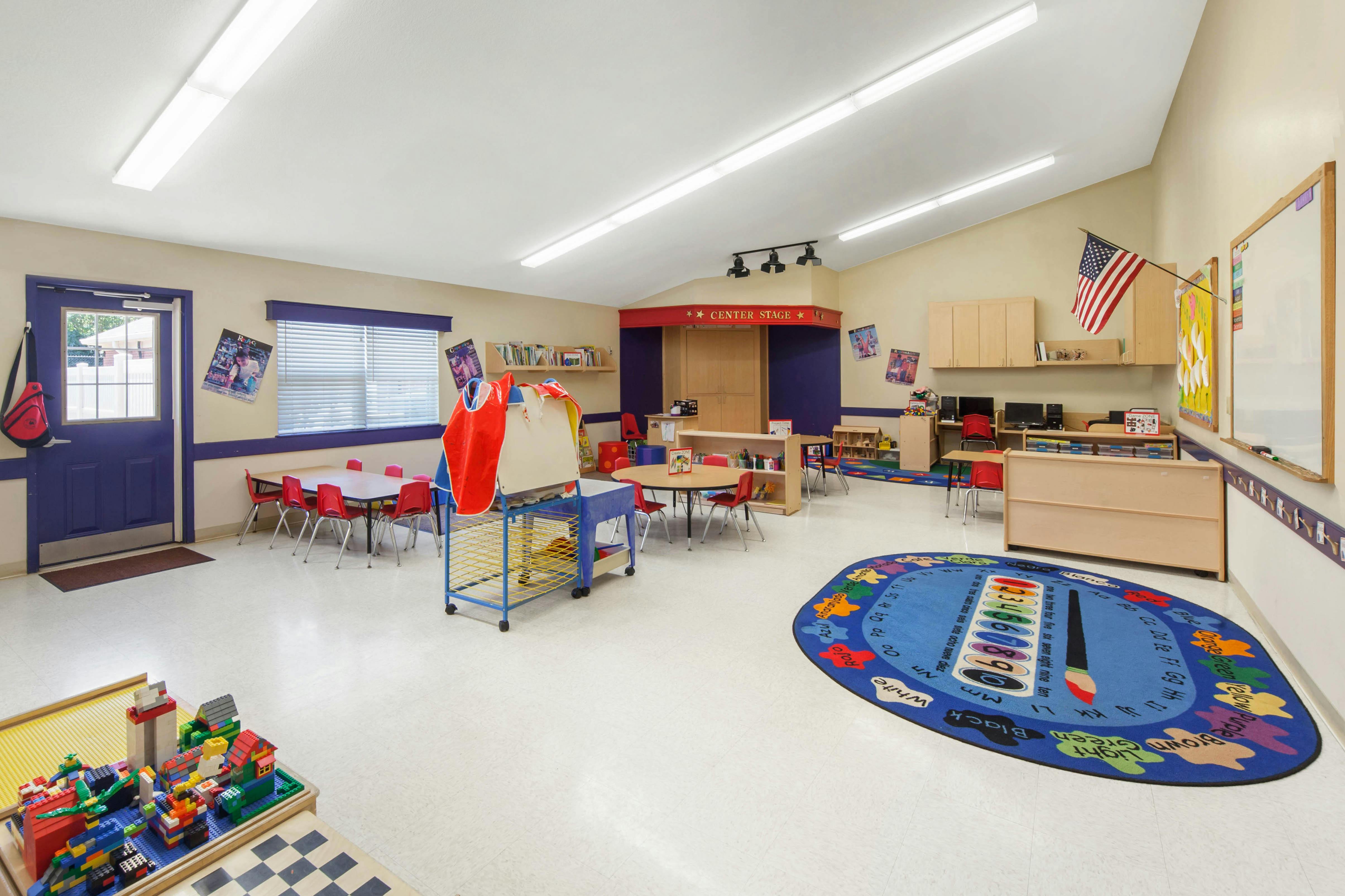 Classroom with tables and chairs, a play area, and an alphabet rug