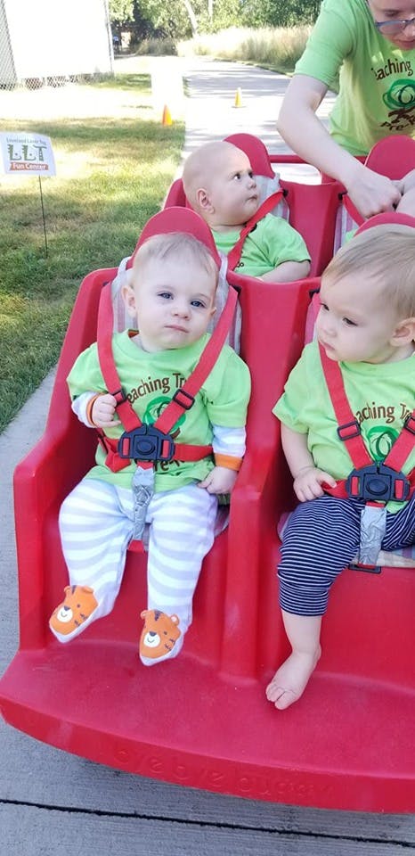 Three children in red seats with a person standing behind them