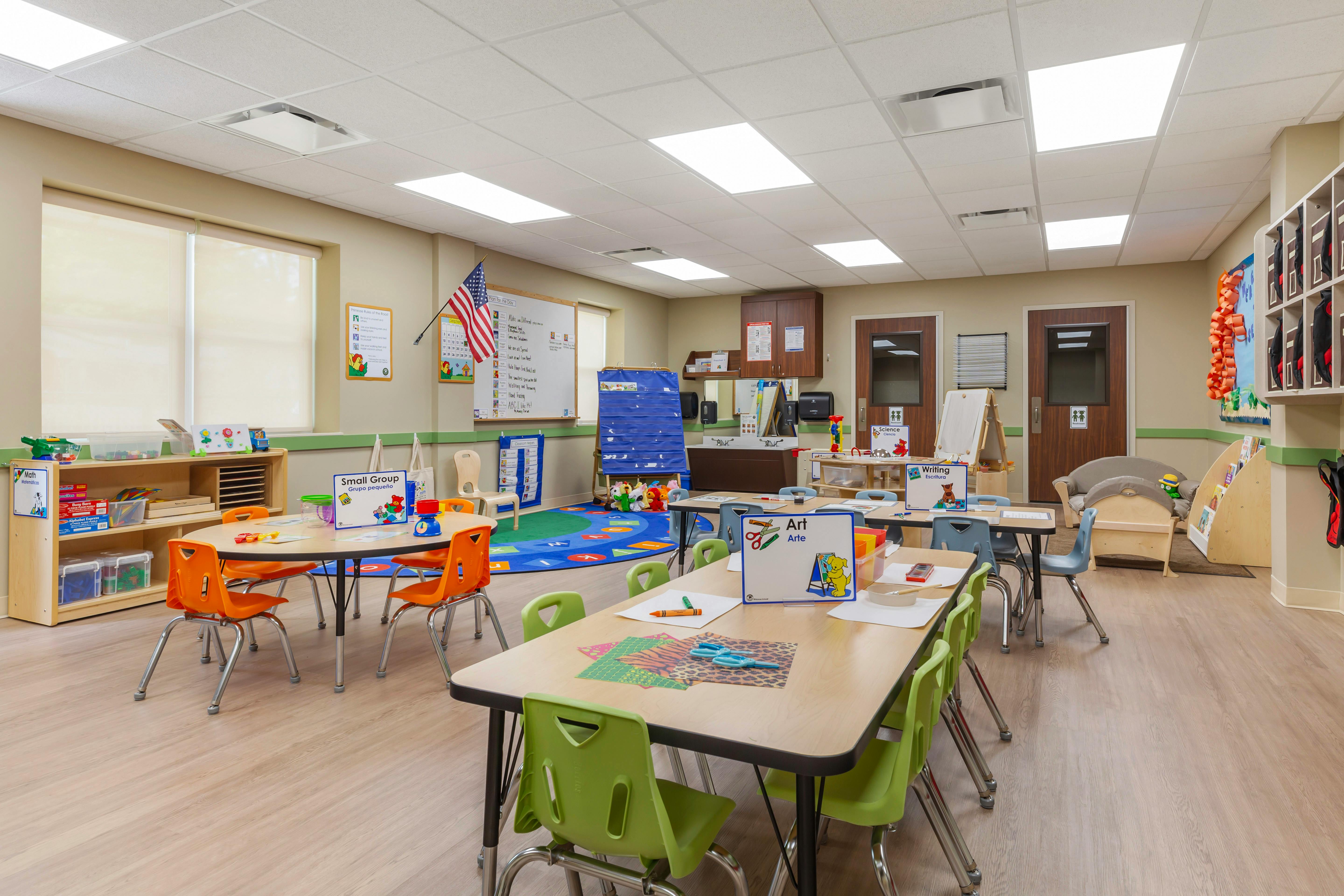 Classroom with small tables and chairs, a whiteboard, and activity signs