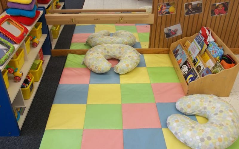 Colorful mat on the floor with two crescent-shaped pillows, a bookshelf, and shelves