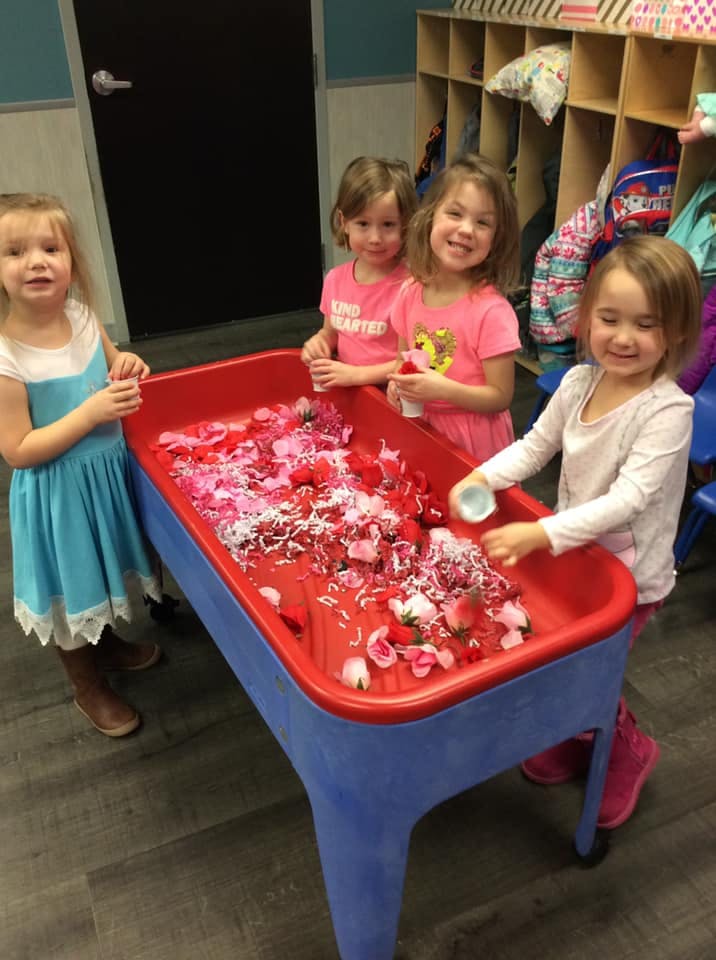 Four children playing with a sensory table filled with red and pink items