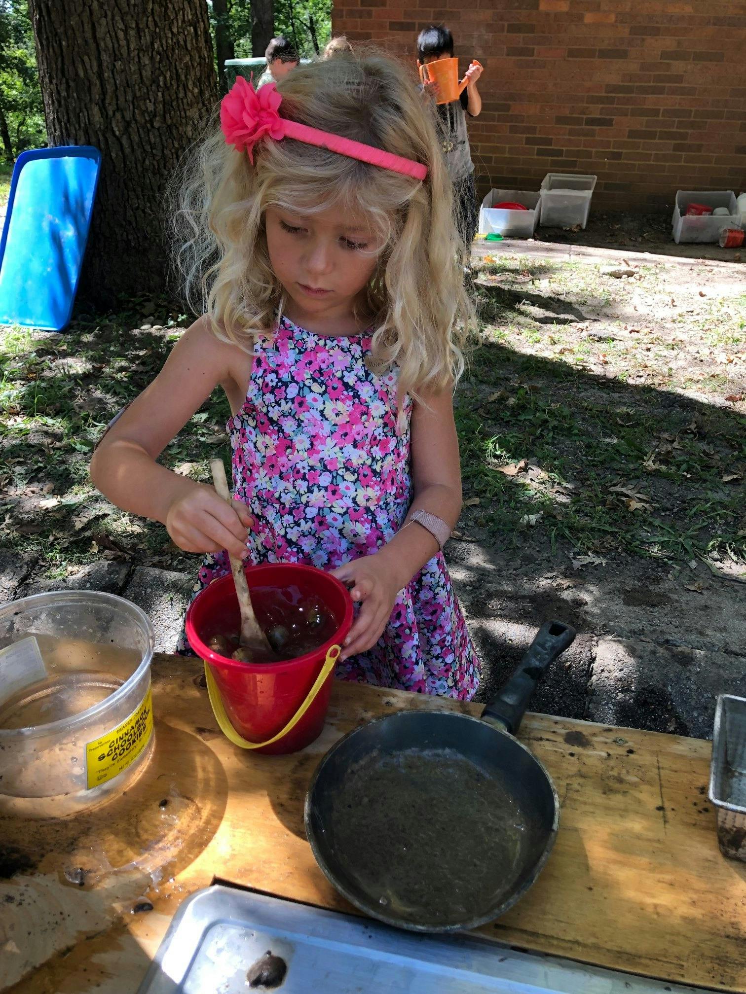 Child stirring contents of a red bucket with a wooden spoon