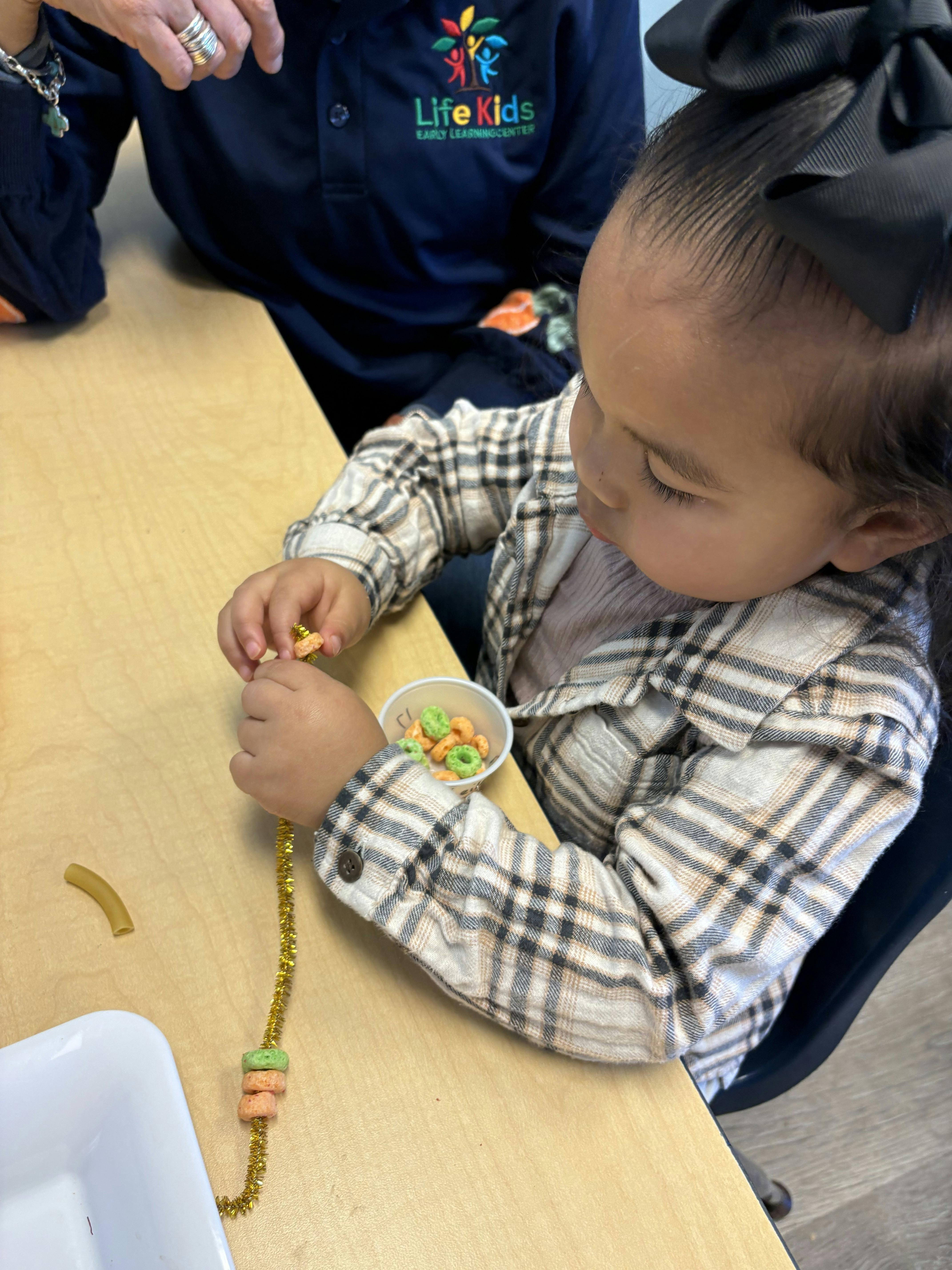 Child threading cereal onto a pipe cleaner at a table