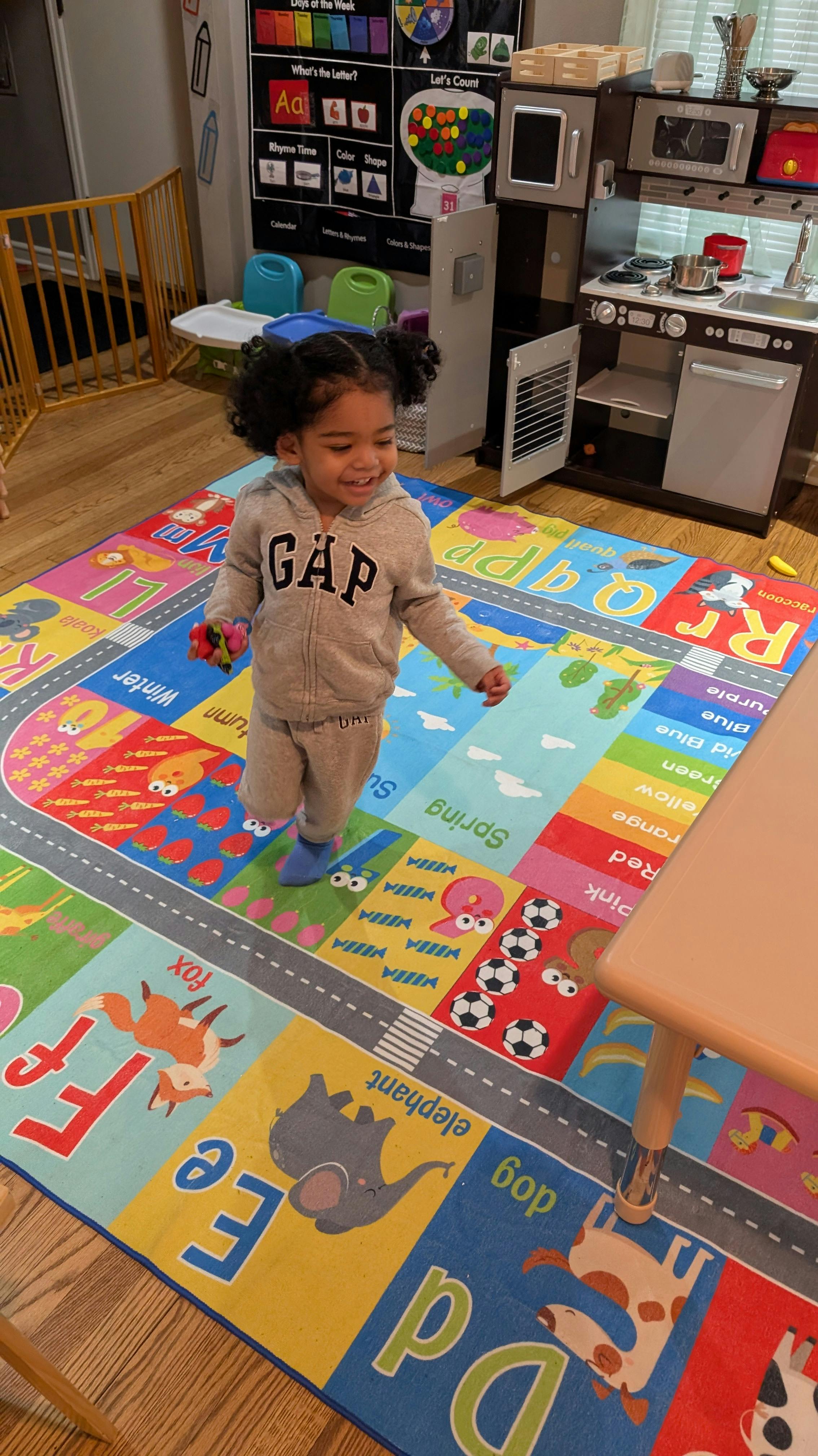 Child standing on a colorful alphabet rug in a play area