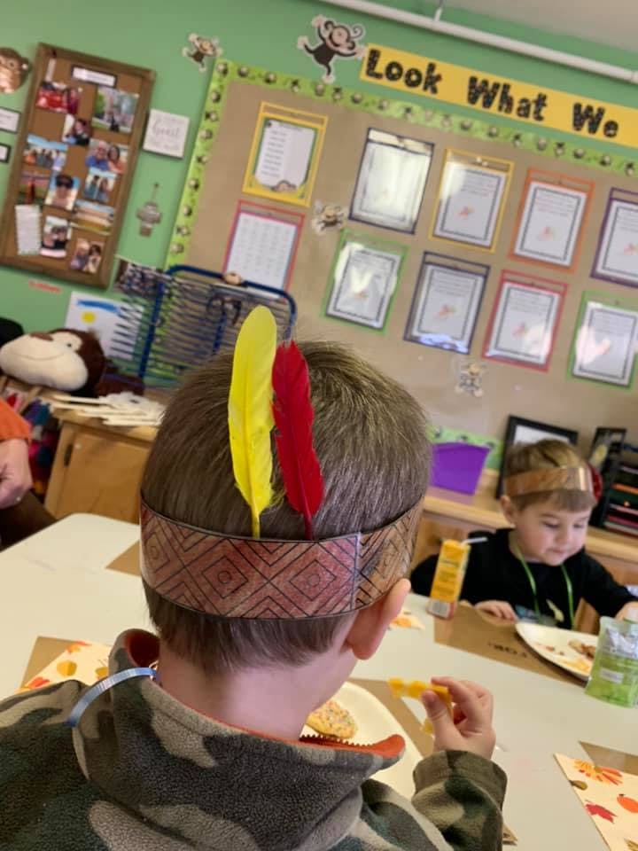 Child wearing a feather headband eating at a table