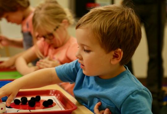 Child playing with small black pom-poms on a red tray