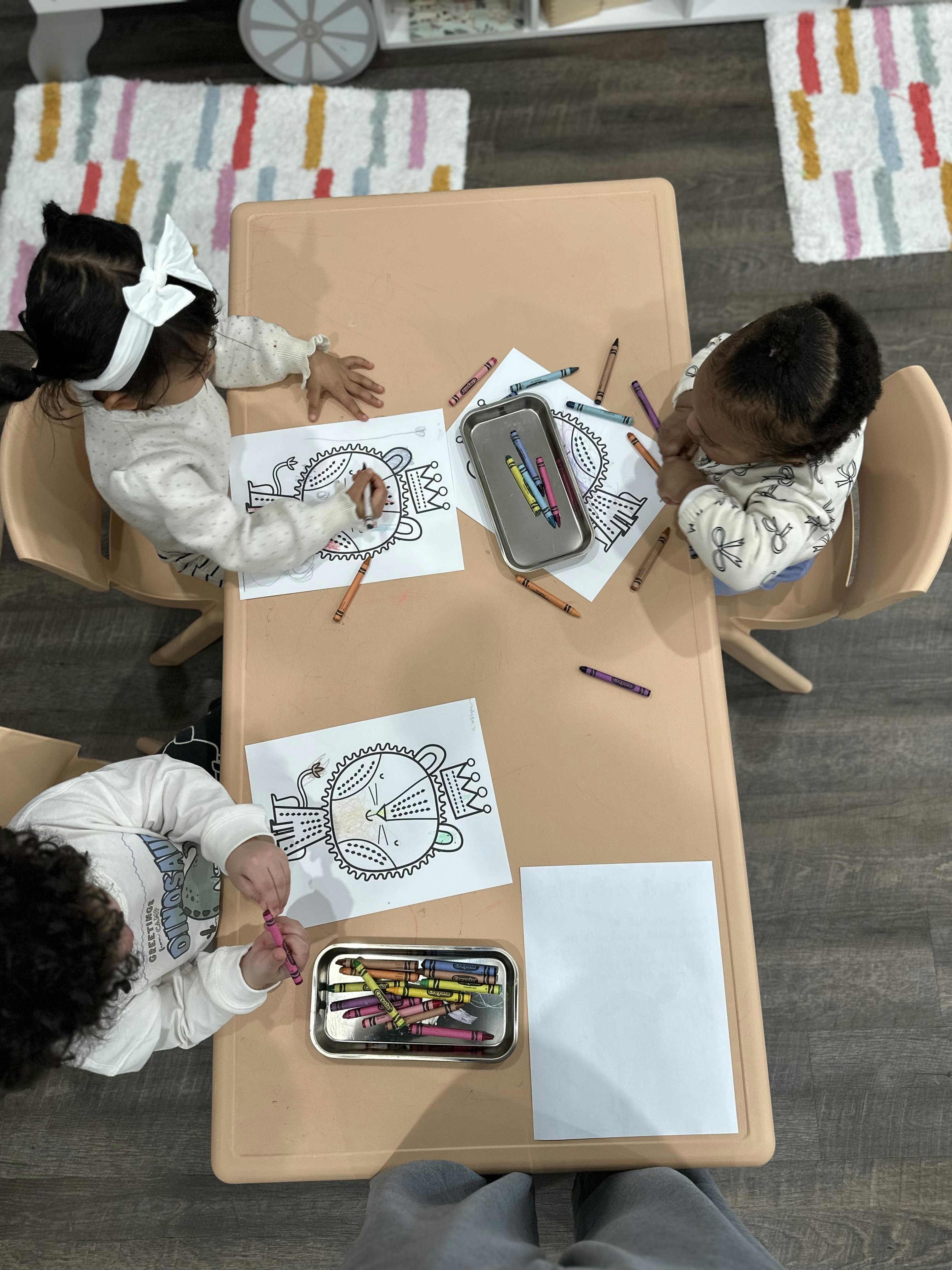 Three children sitting at a table coloring lion drawings with crayons