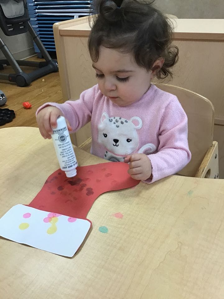 Child decorating a paper stocking with a paint bottle