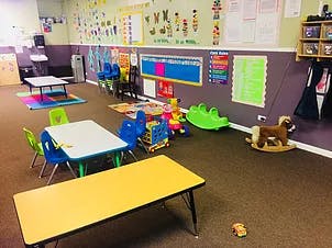 Classroom with small tables and chairs, toys on the floor
