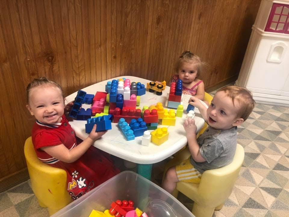 Three children playing with colorful building blocks at a small table
