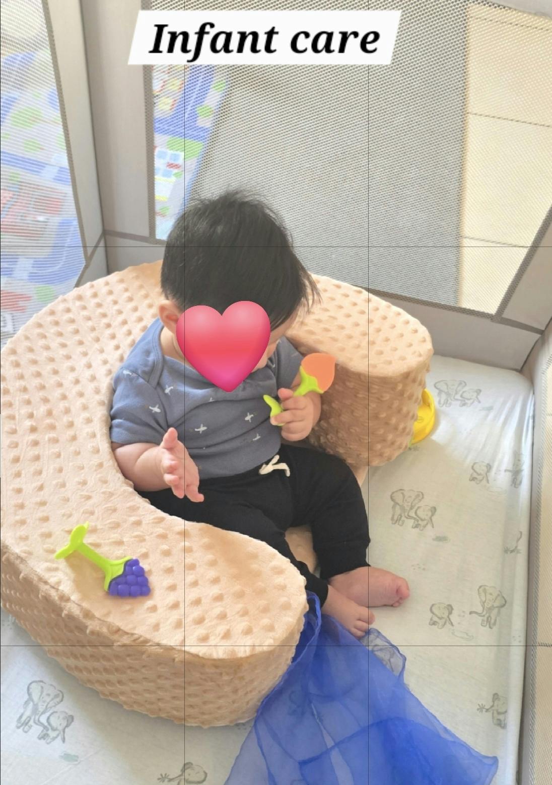 Child sitting in a cushioned floor seat holding a toy in a playpen