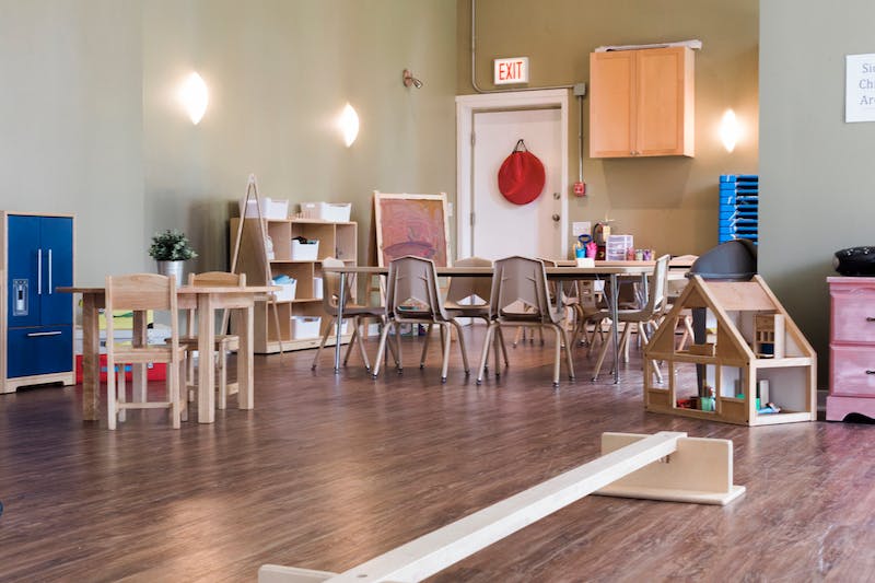 Empty classroom with small tables and chairs, play kitchen, and dollhouse