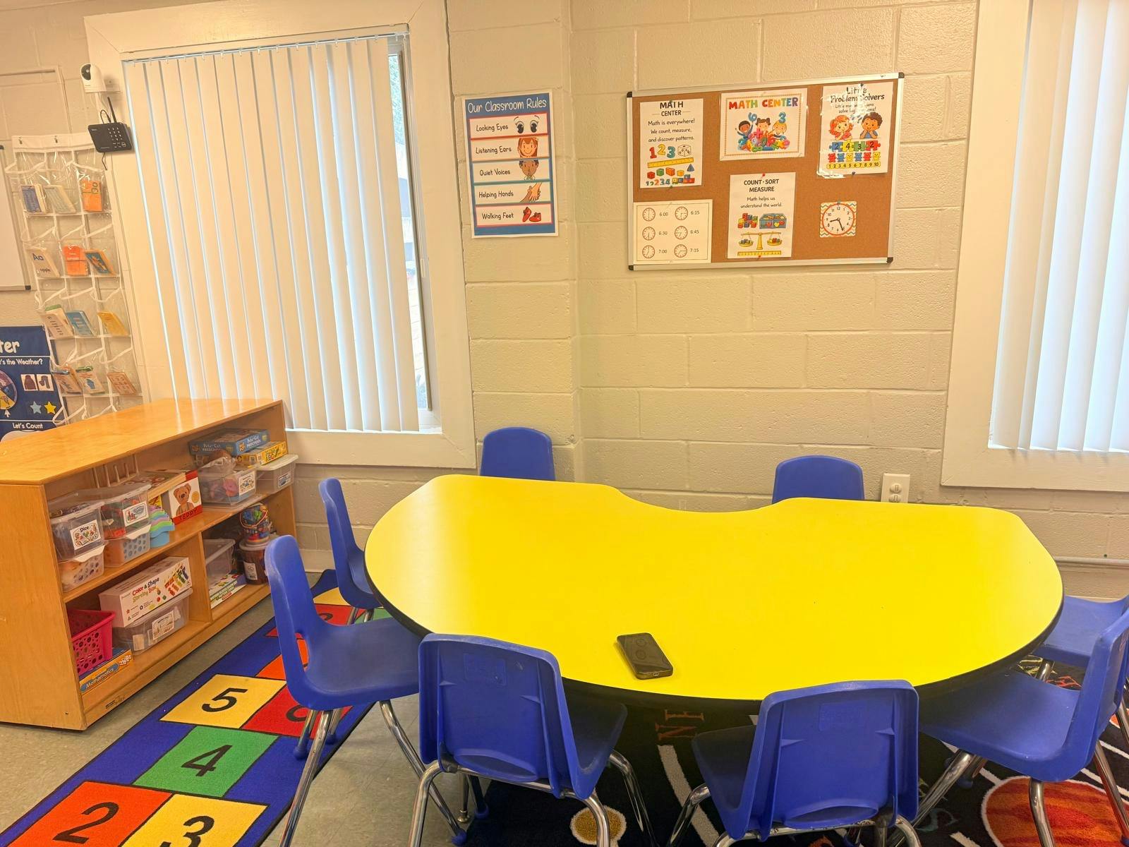 Classroom math center with a yellow kidney-shaped table and blue chairs