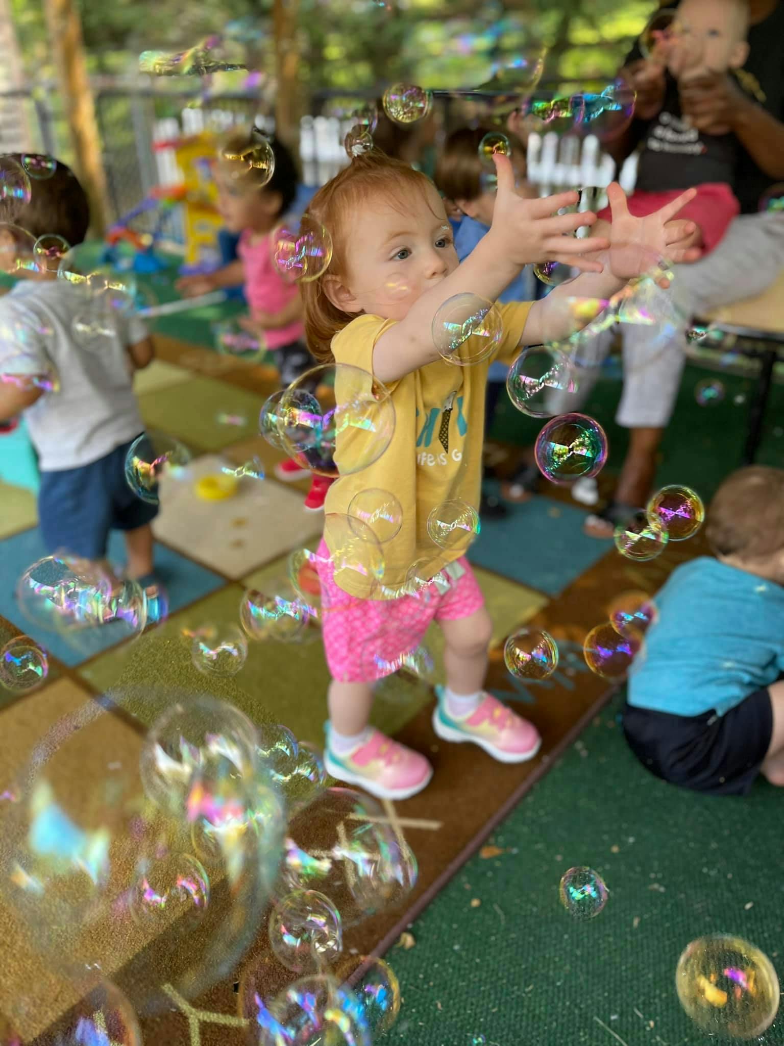 Child reaching for bubbles with other children in the background