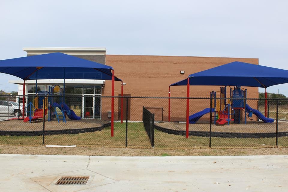 Two fenced playgrounds with blue shade structures and slides