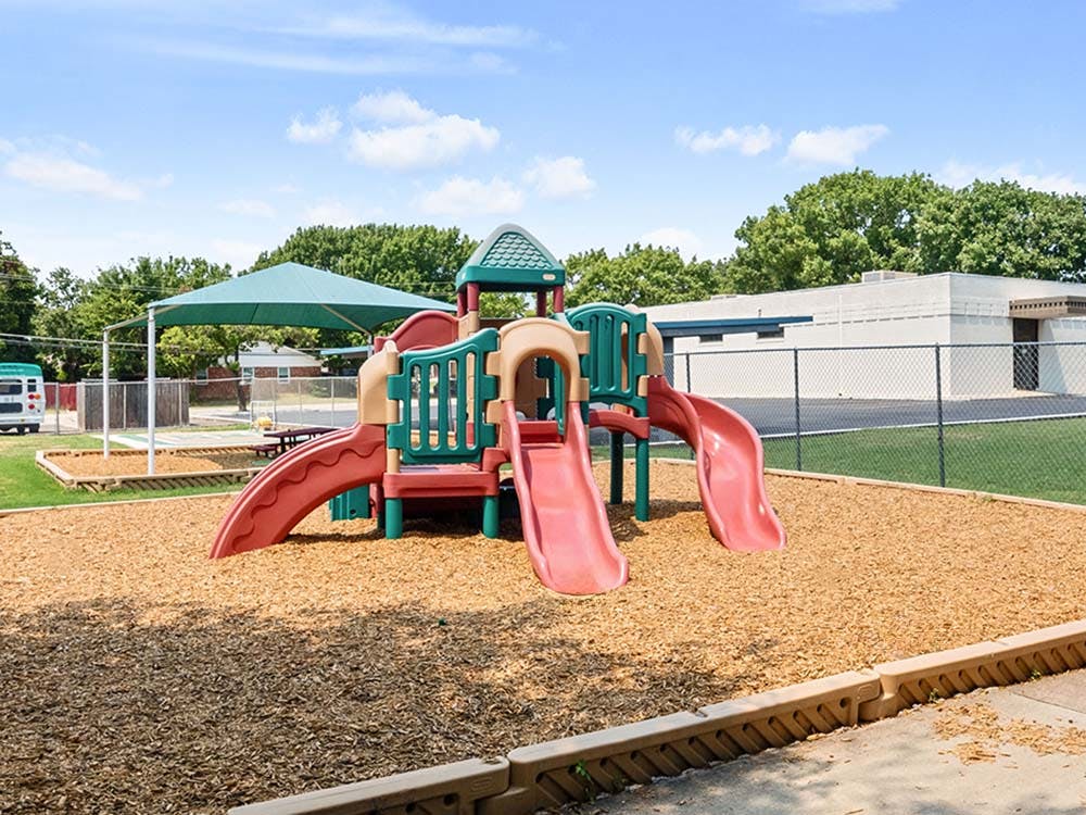 Empty playground with slides and wood chips under a shaded area