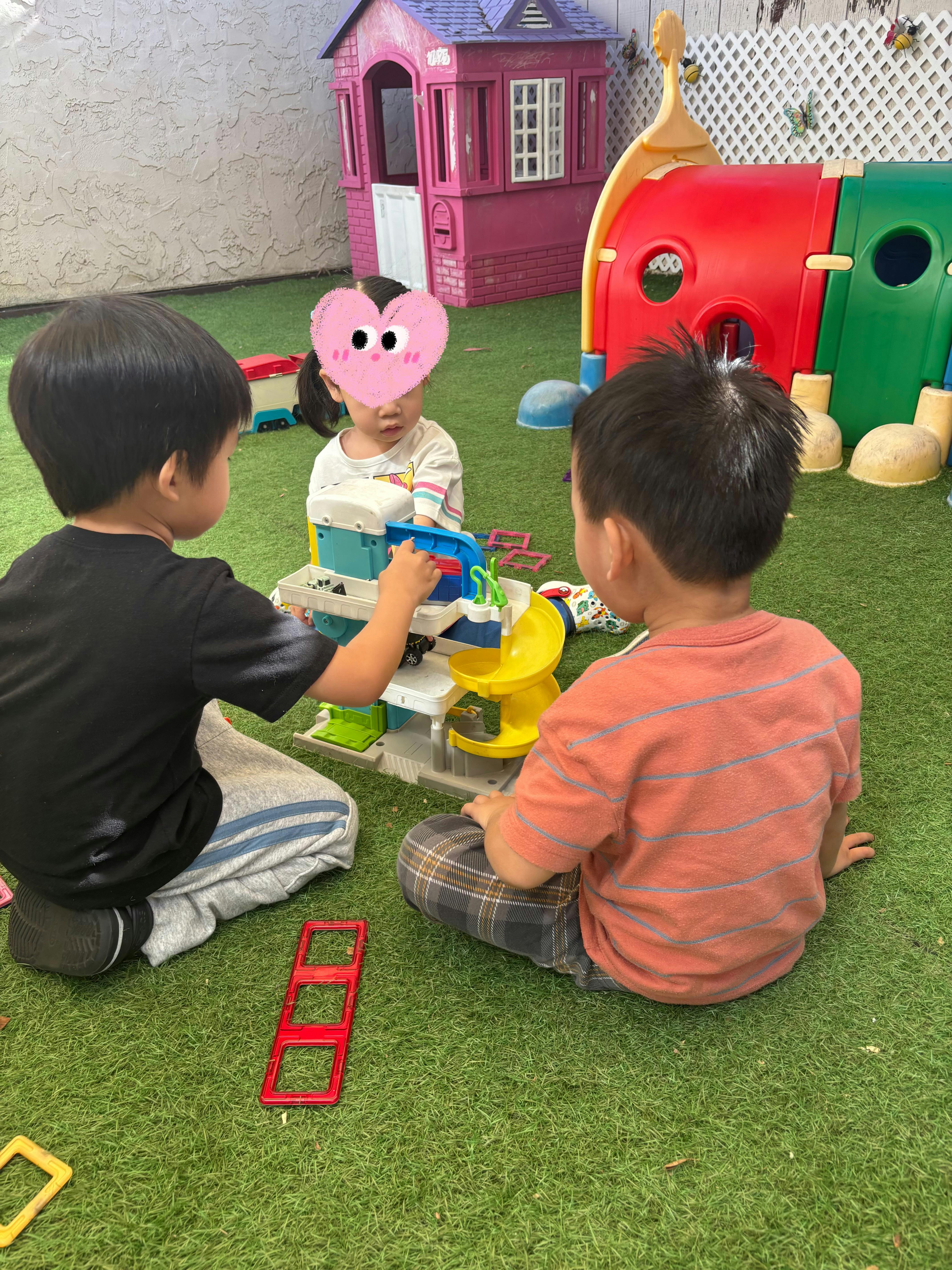 Three children playing with a toy car ramp on artificial grass