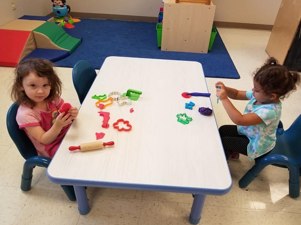 Two children playing with playdough and cookie cutters at a table