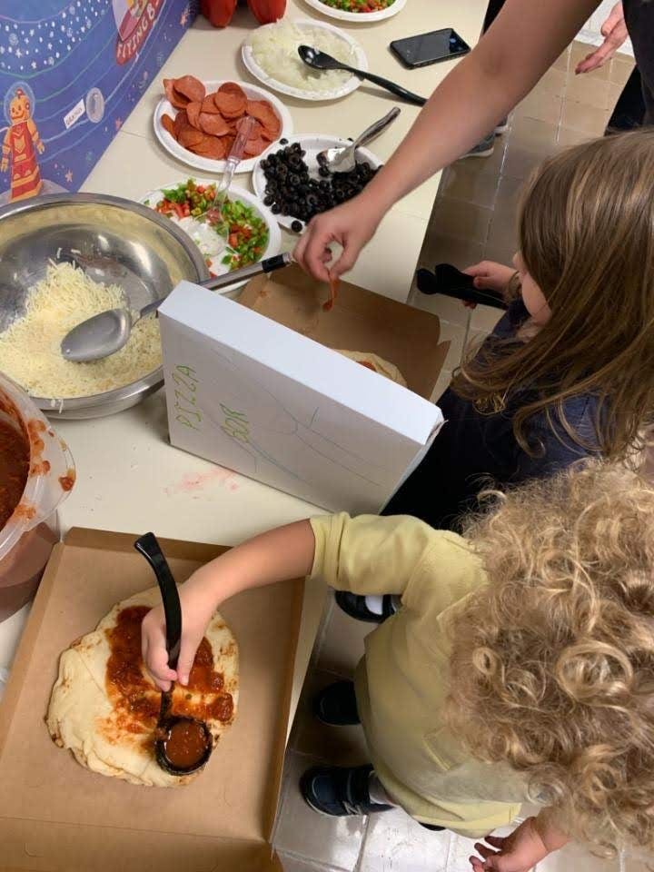 Two children making pizzas with various toppings on a table