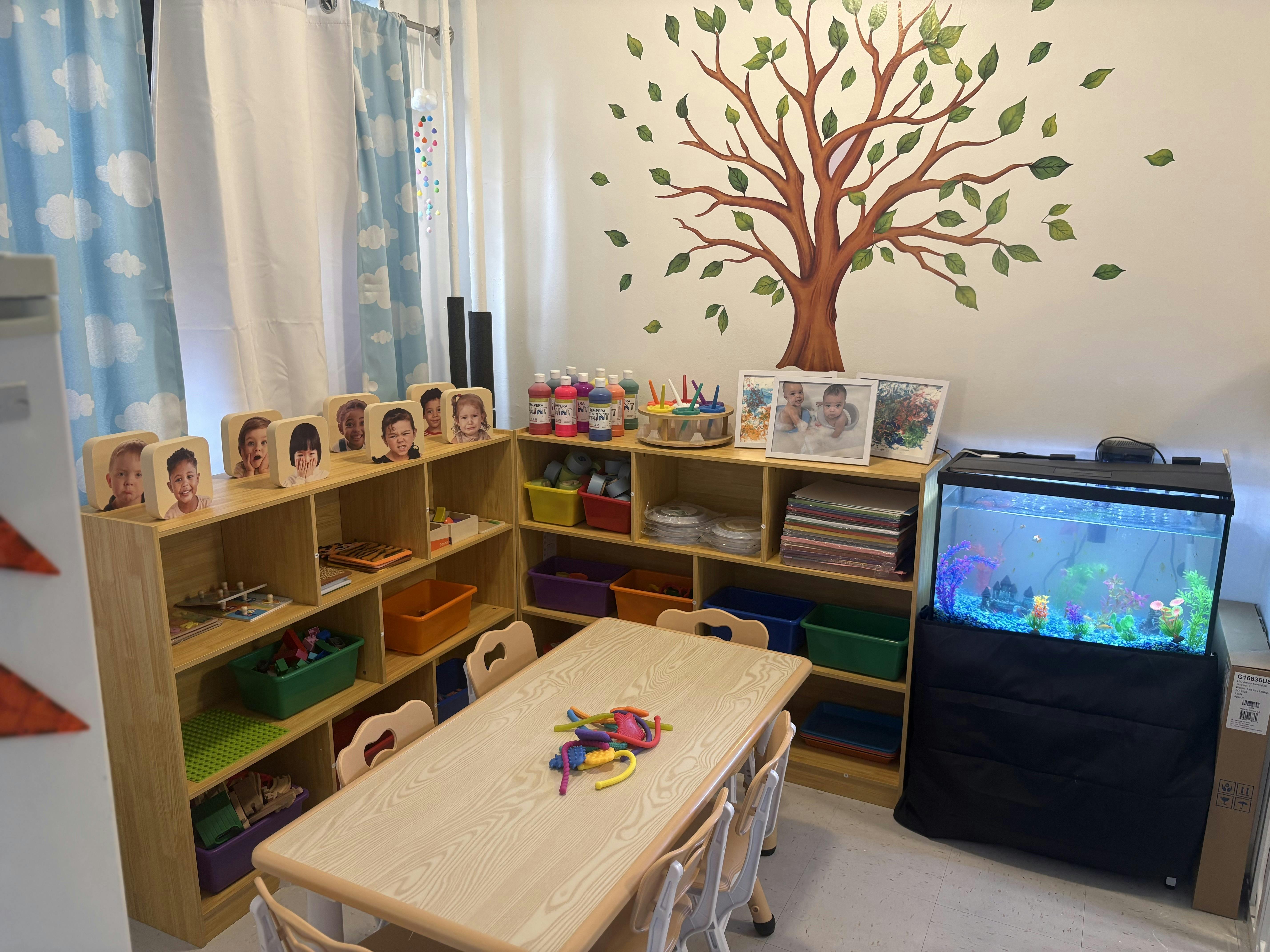 Childcare room with wooden shelves, small chairs and table, and a fish tank