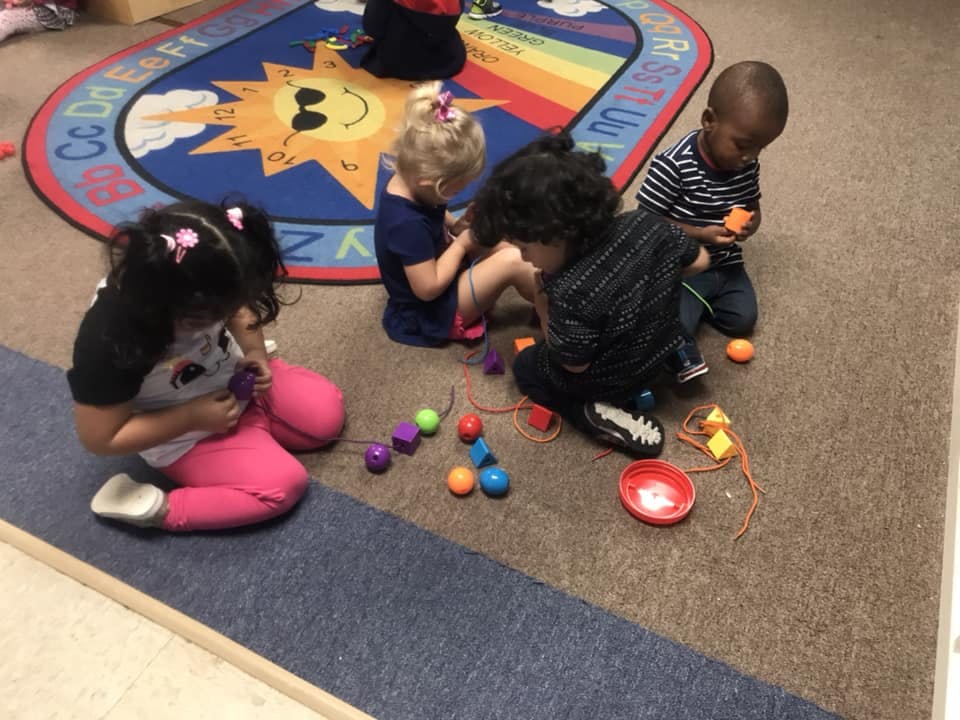 Four children playing with colorful blocks and beads on a rug