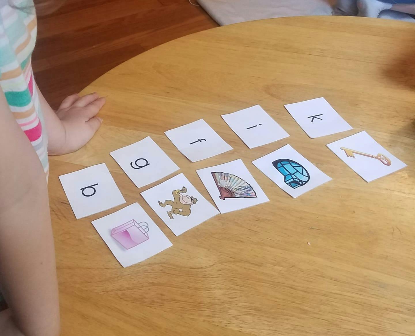 Child's hand next to cards with letters and images on a wooden table